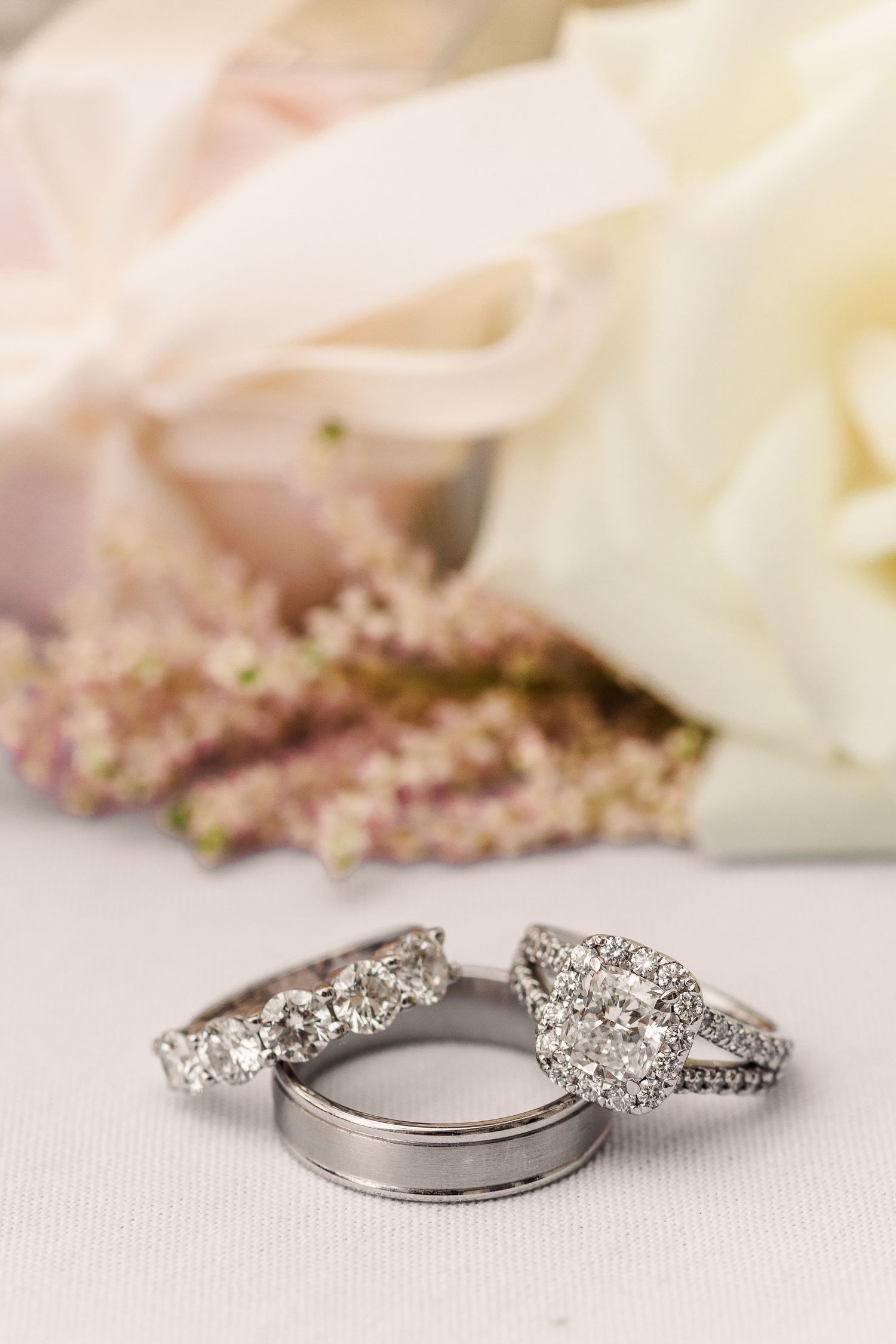 Diamond wedding ring set photographed against white flower petals and soft pink accents.