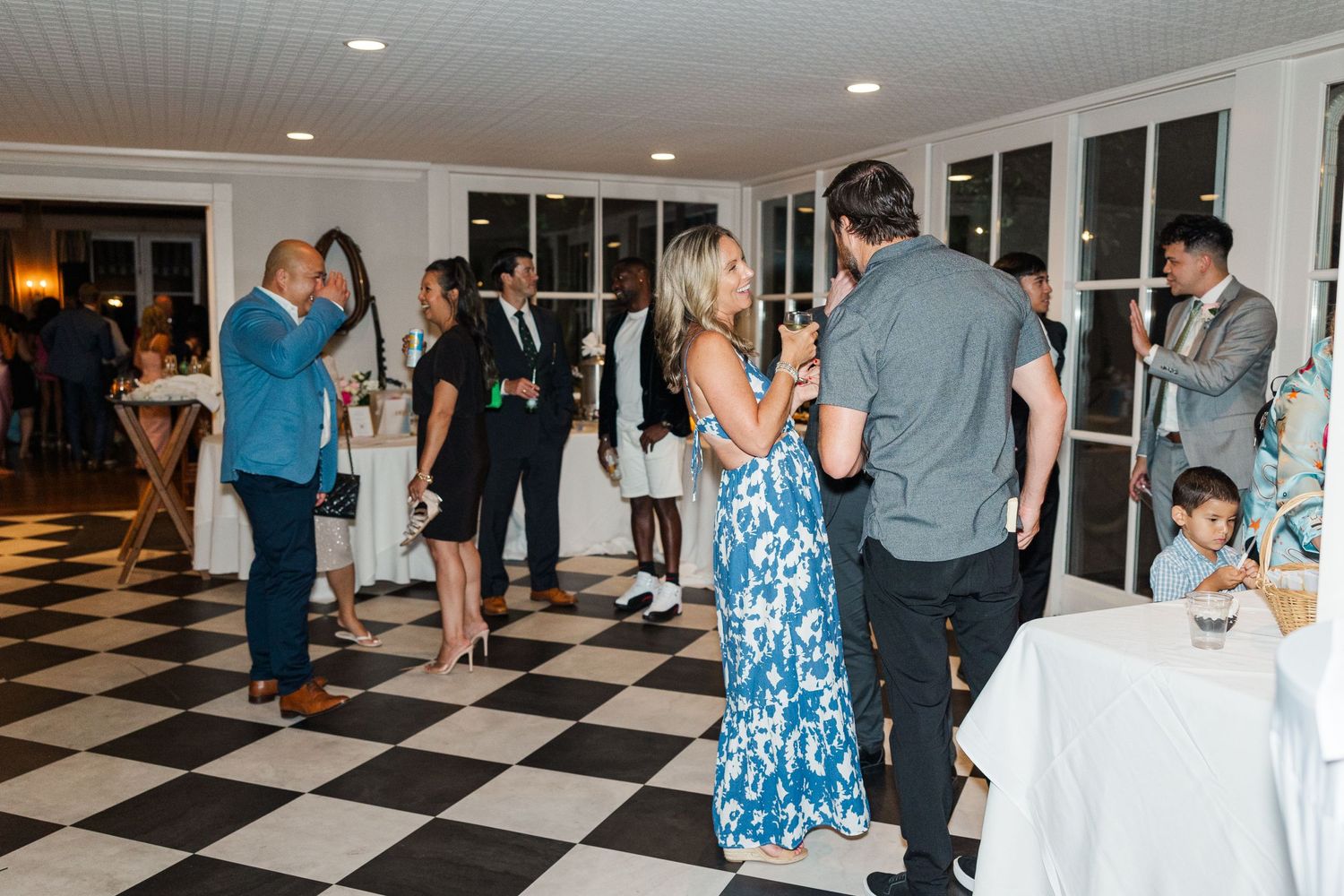 Wedding guests mingle and socialize on a black and white checkered floor during an elegant evening reception.