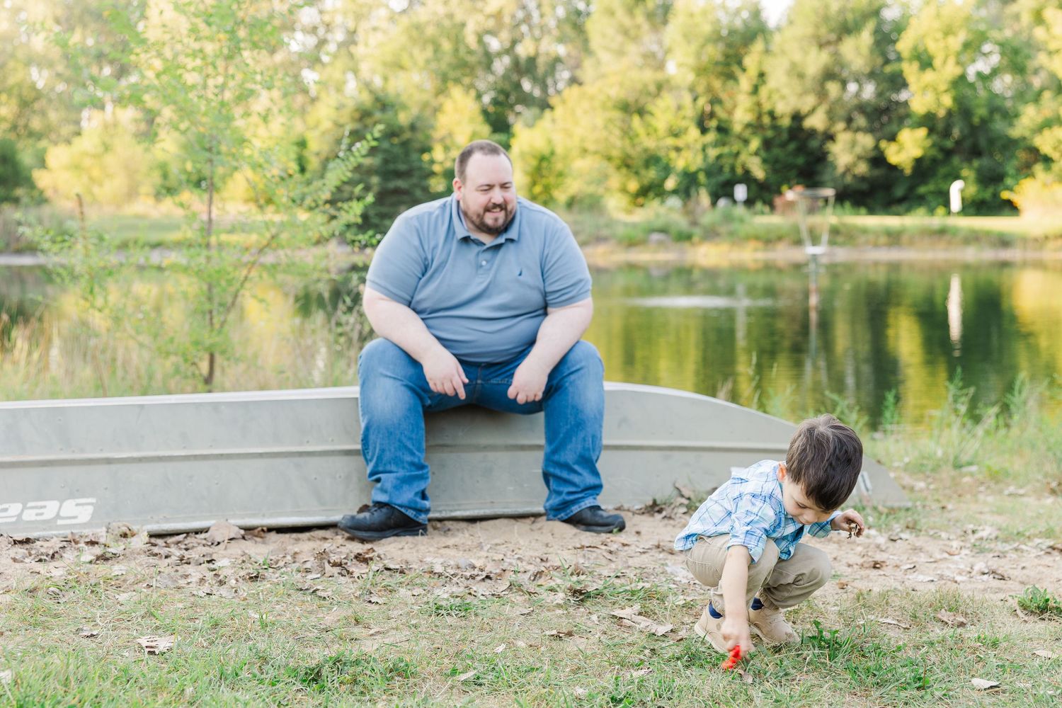 People relax together on stone ledge in park during autumn with colorful trees and lake in background.Sorg family portraits at Shamrock Hill
