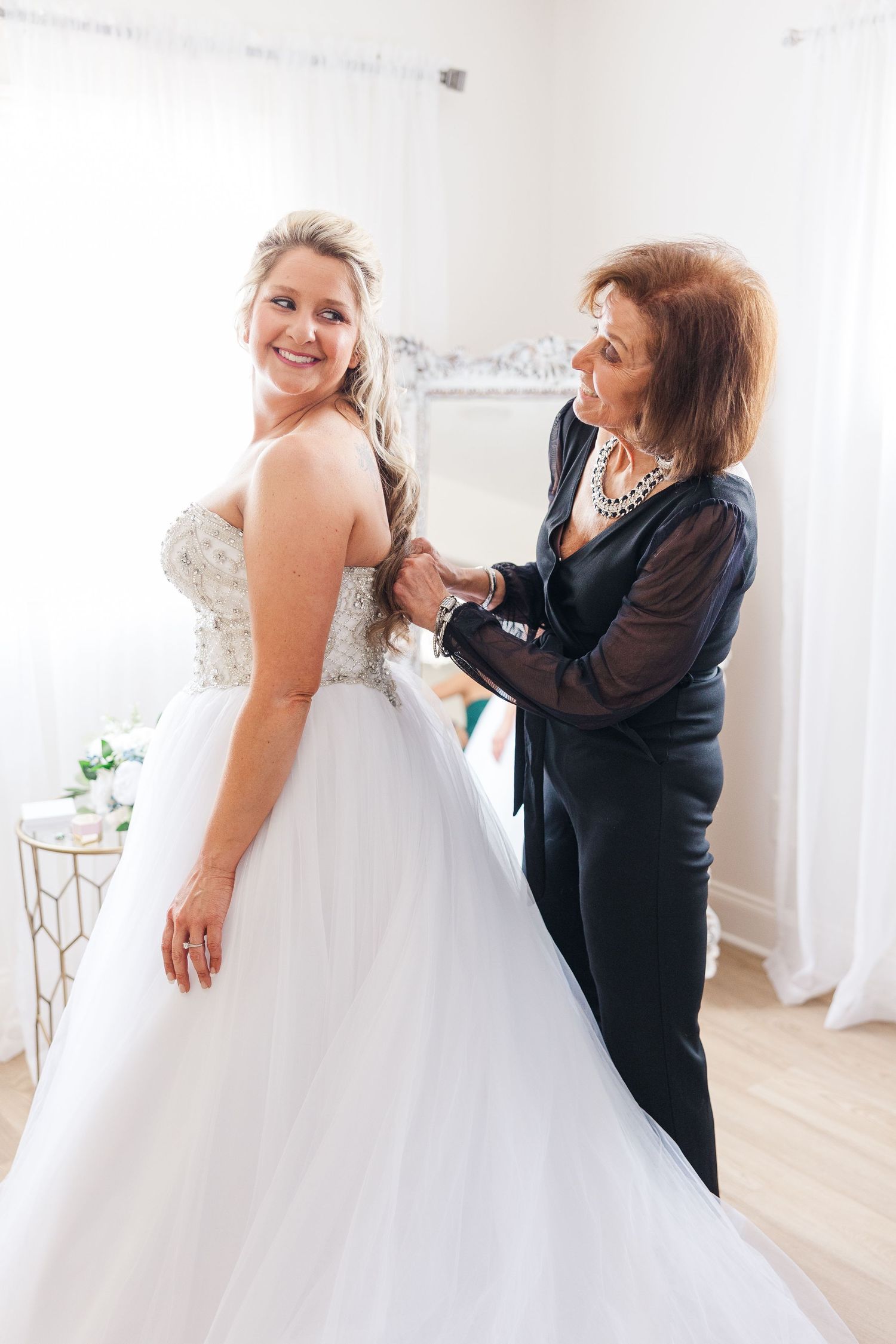 A beautiful wedding gown being adjusted in a bright white room with elegant decor.
