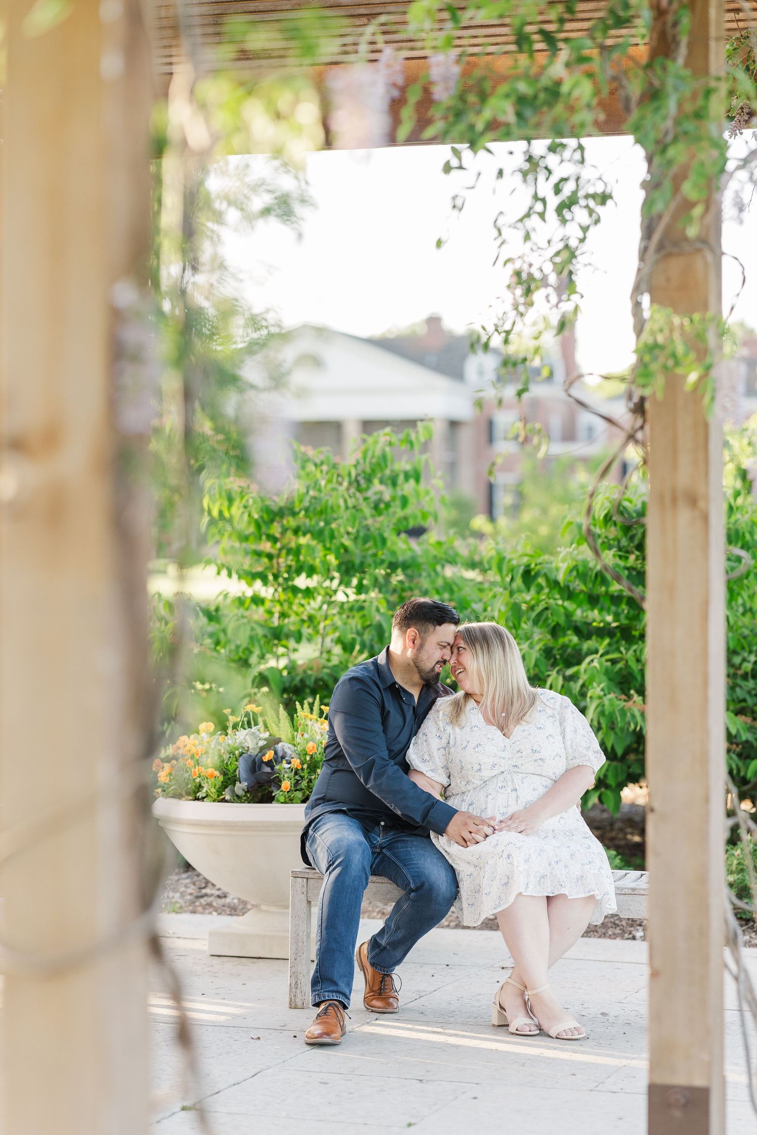 A couple shares a romantic moment under a pergola framed by green foliage.