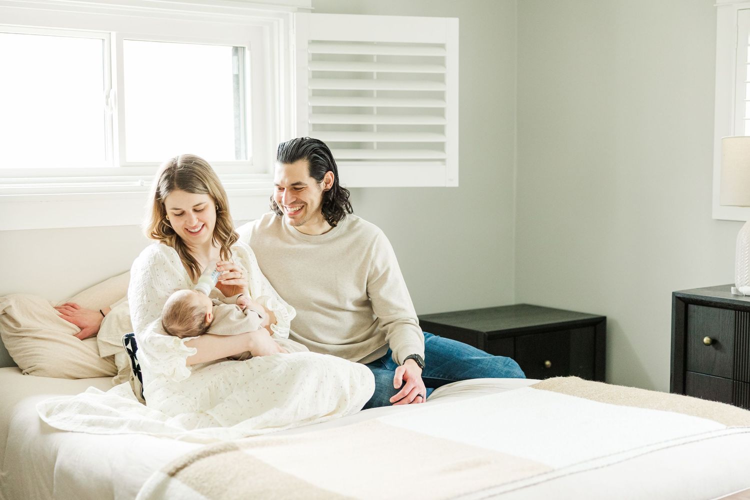 Mother and father sitting on their bed with their newborn baby during an in-home lifestyle newborn session in Palatine Illinois