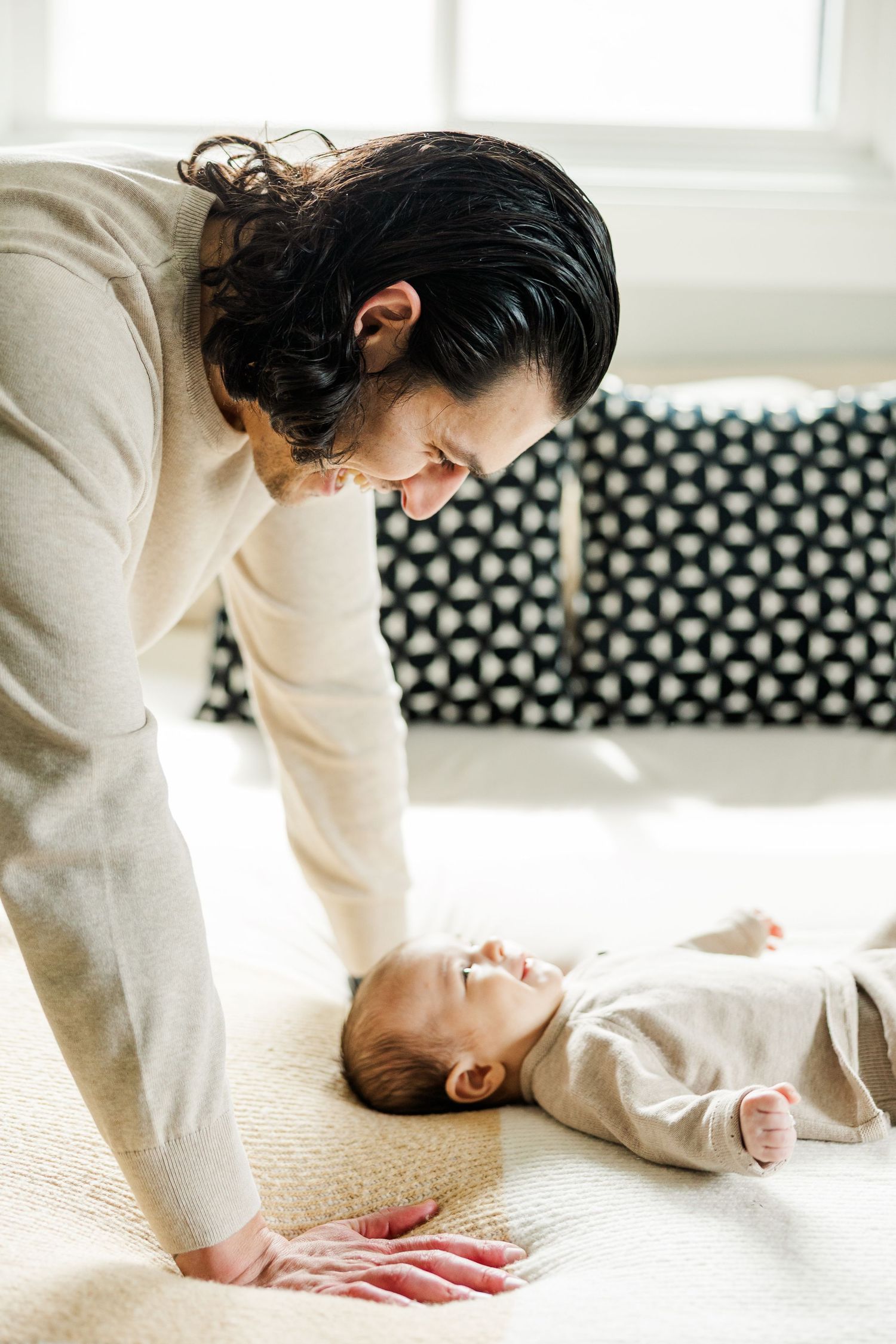 Father leaning over and smiling at his newborn baby on a bed during an in-home lifestyle newborn photography session in Palatine Illinois