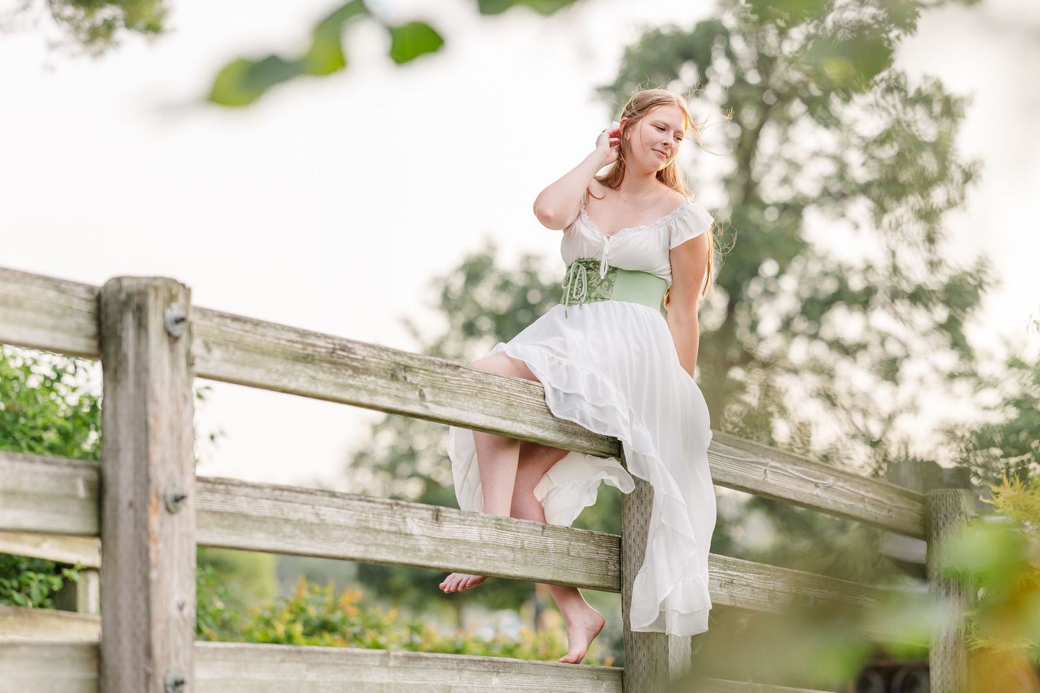 Samantha sits on a wooden bridge in a flowing white dress during her Cantigny Park senior portraits.