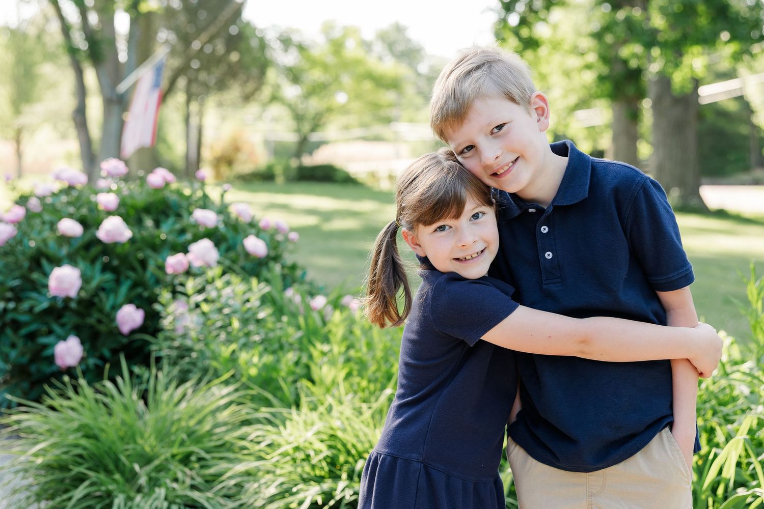 Brother and sister hugging outside in a sunny summer garden for a free summer checklist for kids blog post