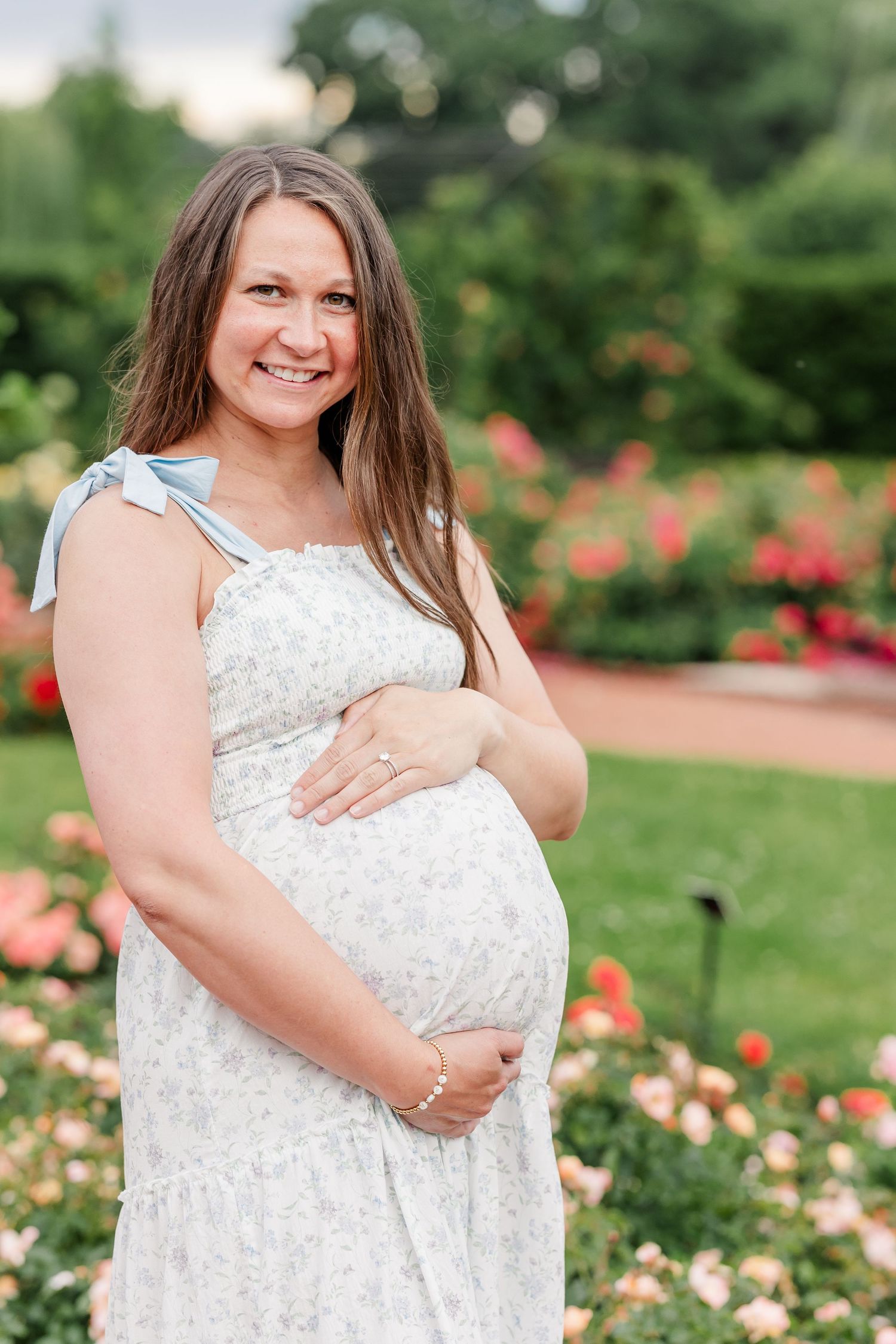 Expecting mother smiling in the summer rose garden during her maternity photos