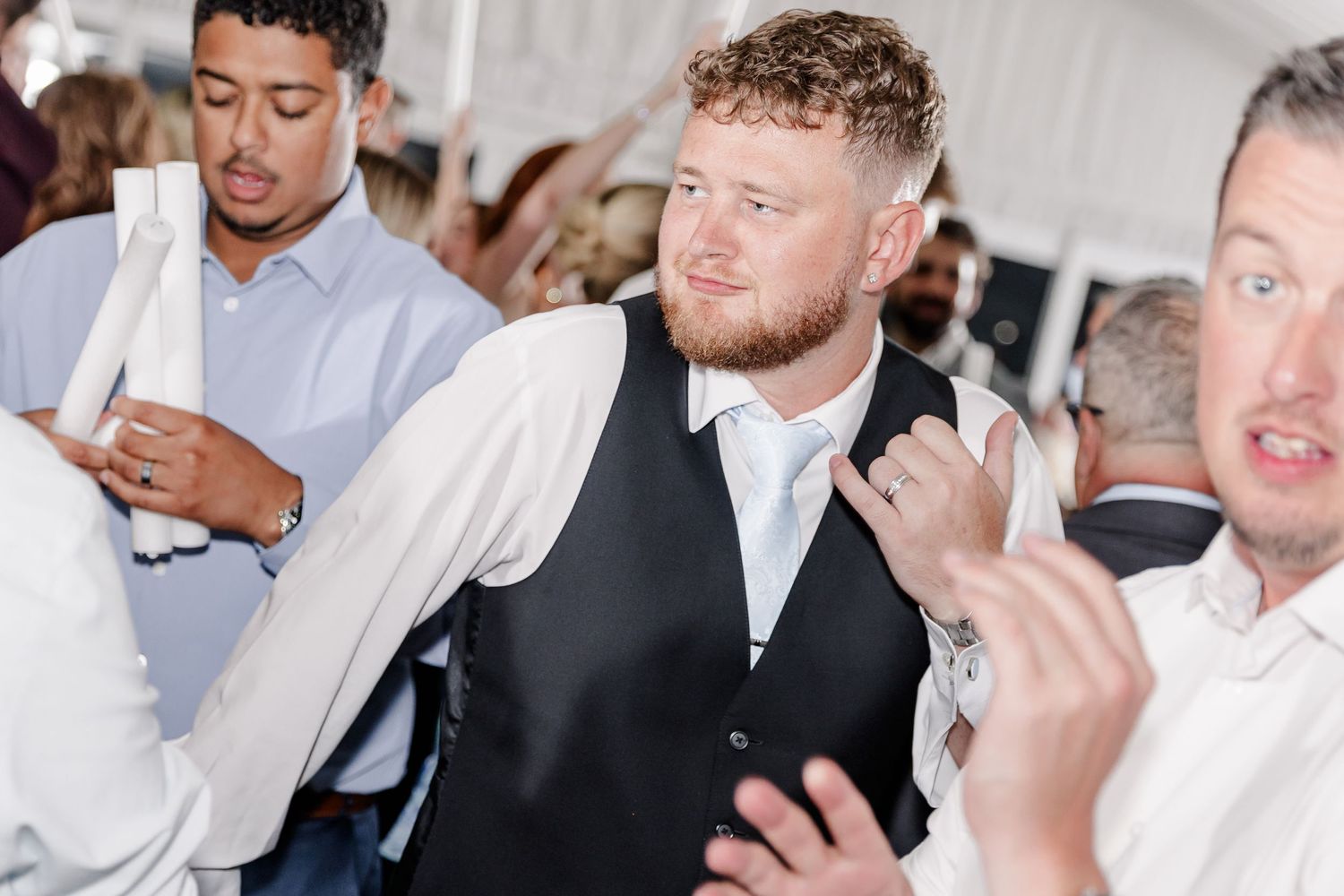 Young man in black vest and white shirt dancing energetically at a lively wedding reception.