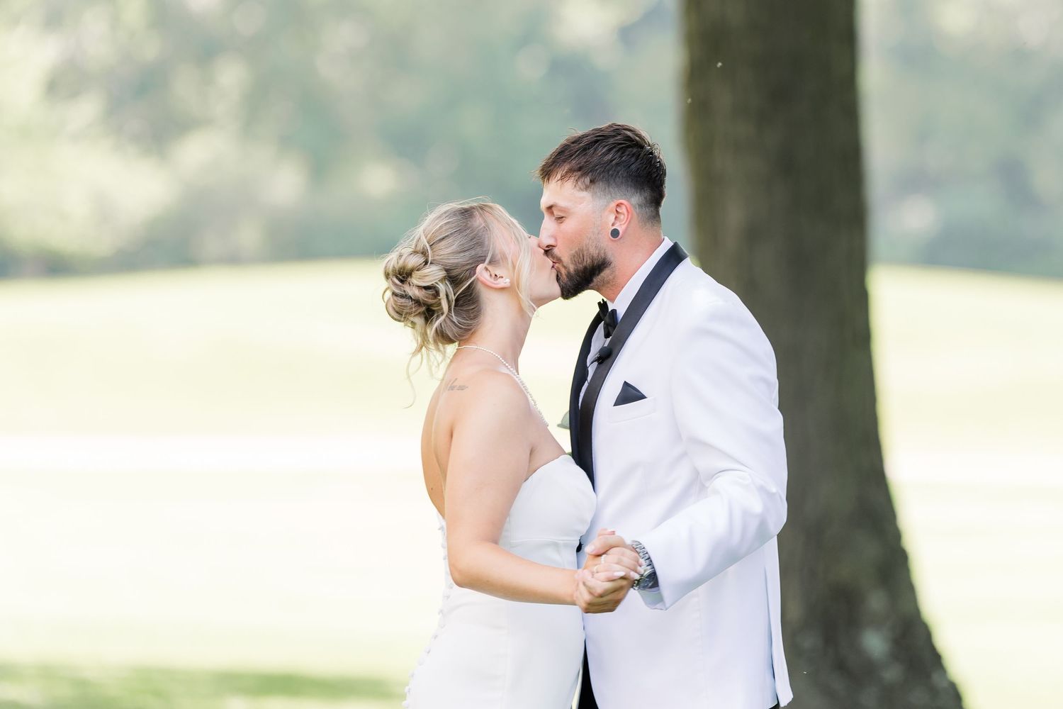 Bride and groom share a romantic almost-kiss under a large tree in soft natural light.