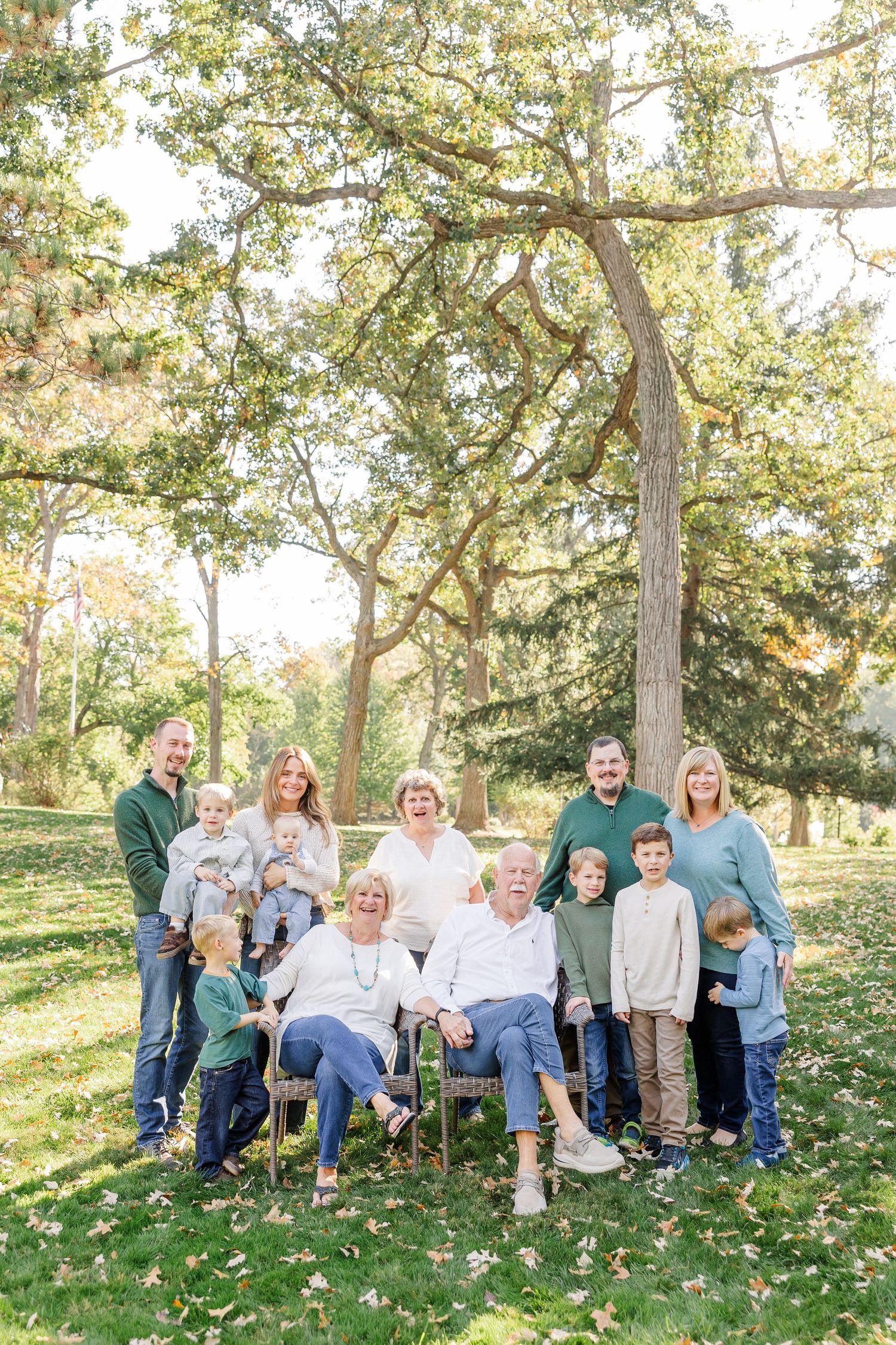 Multi-generational family portrait outdoors in a park with lush green trees during autumn.