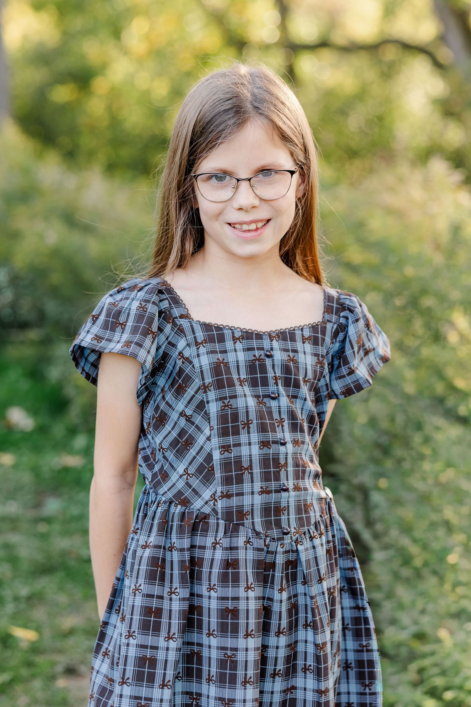 Smiling girl wearing glasses and a plaid dress during fall portraits in St. Charles, IL.