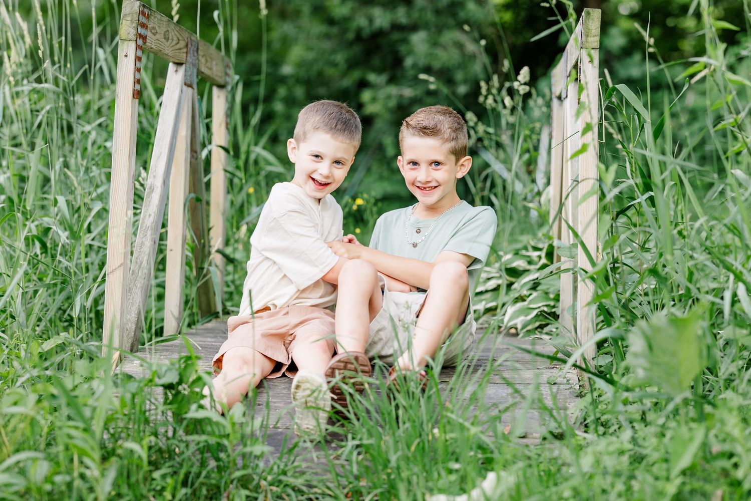 Two brothers sitting together in the greenery during a summer family portrait session in Crystal Lake, Illinois.