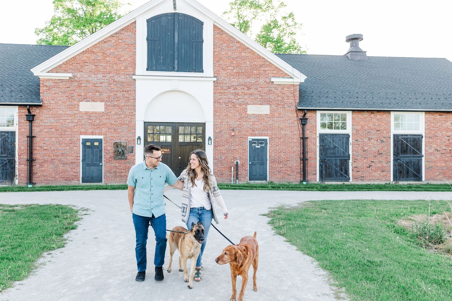 Engaged couple walking their dogs outside the barn at St. James Farm Preserve