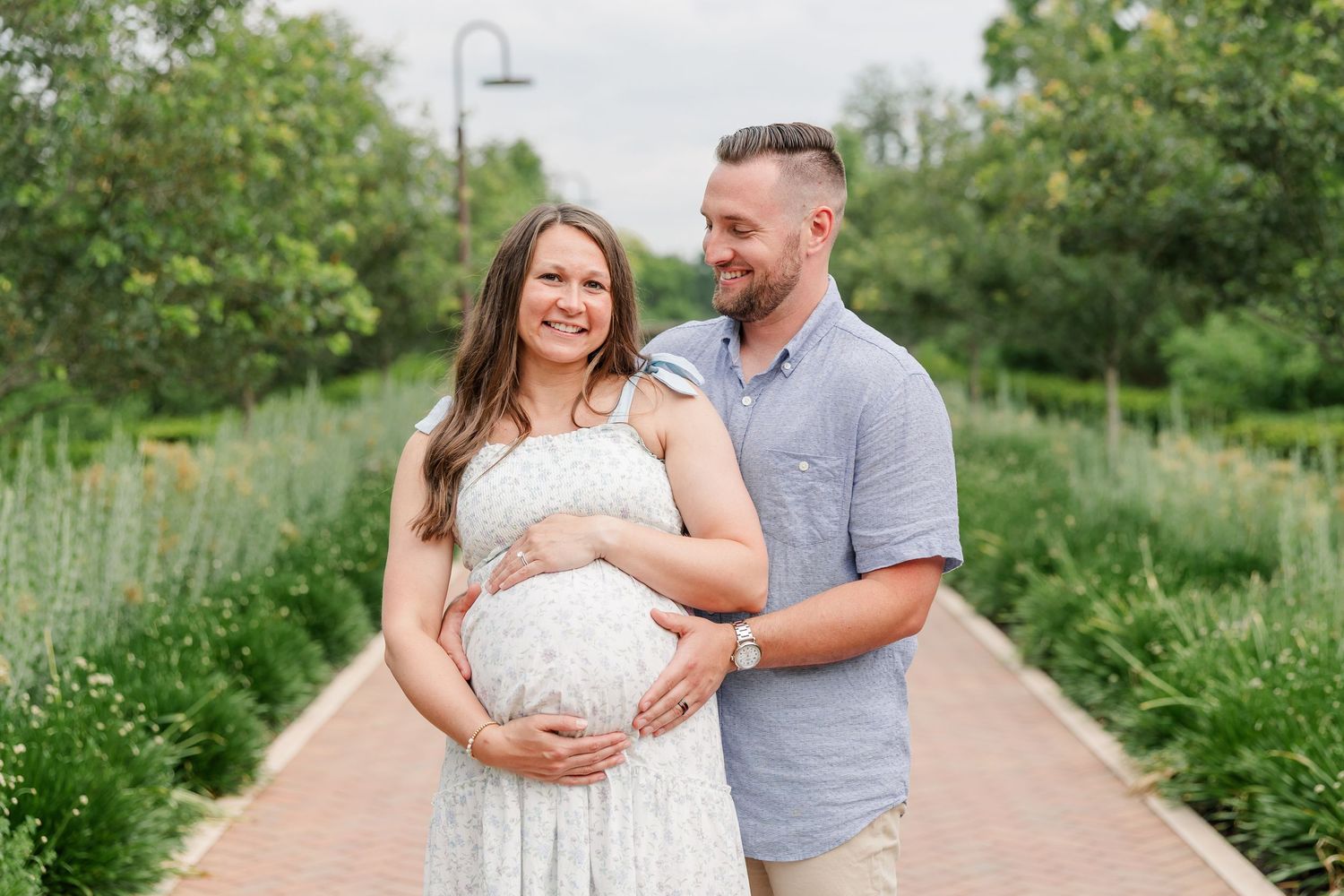 Expecting parents smiling together on a garden path during their maternity session