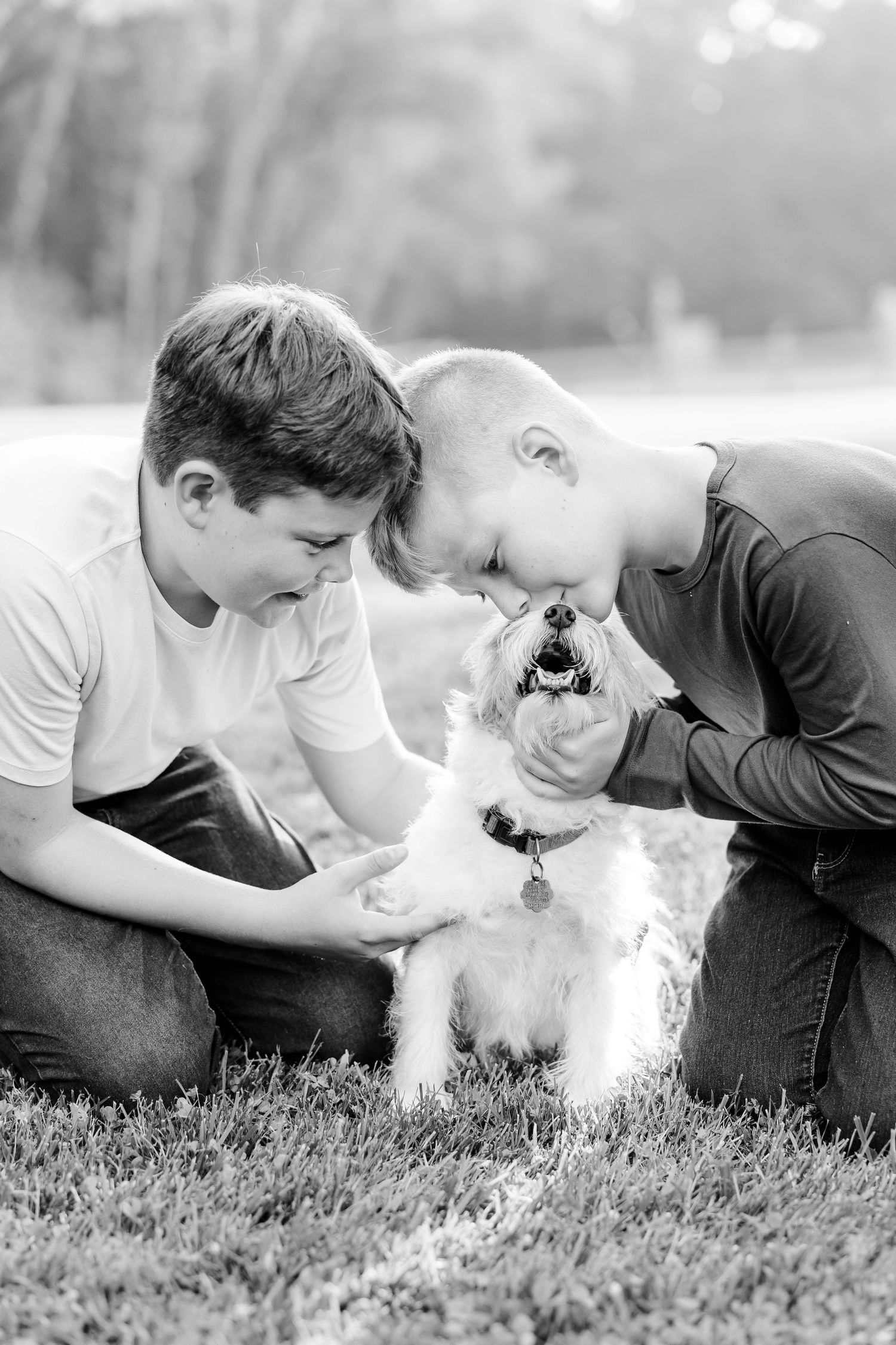 Two brothers cuddling with their family dog in a black and white portrait.