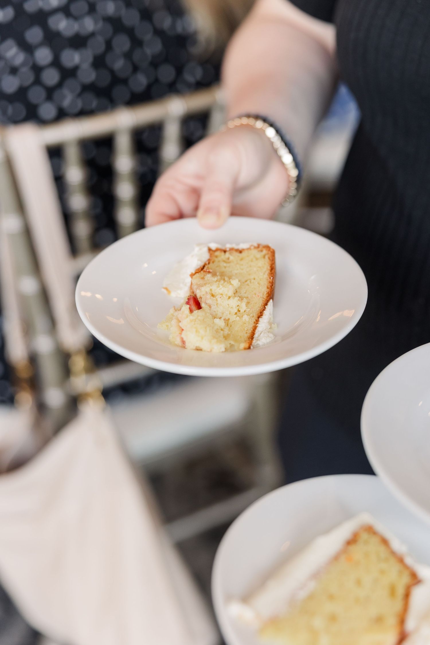 Hand holding a white plate with a slice of white cake with strawberry filling at a wedding reception.