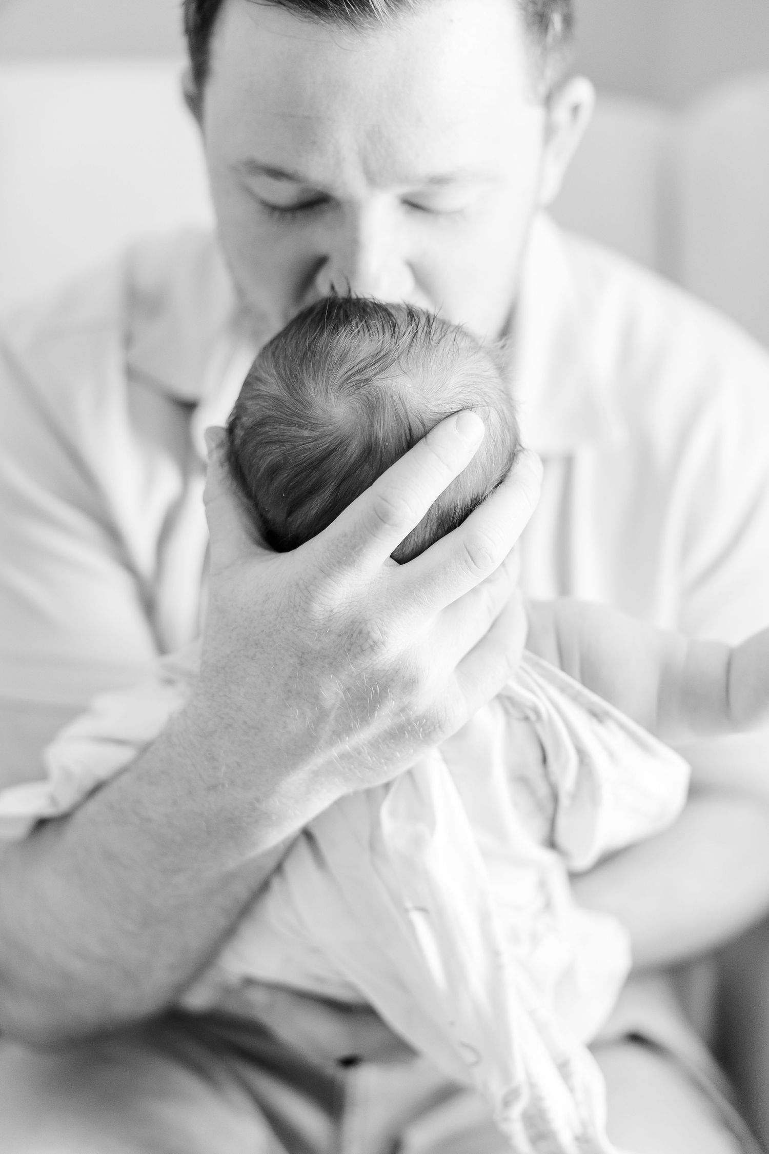 Black and white photo of dad kissing newborn baby girl during an in-home newborn session