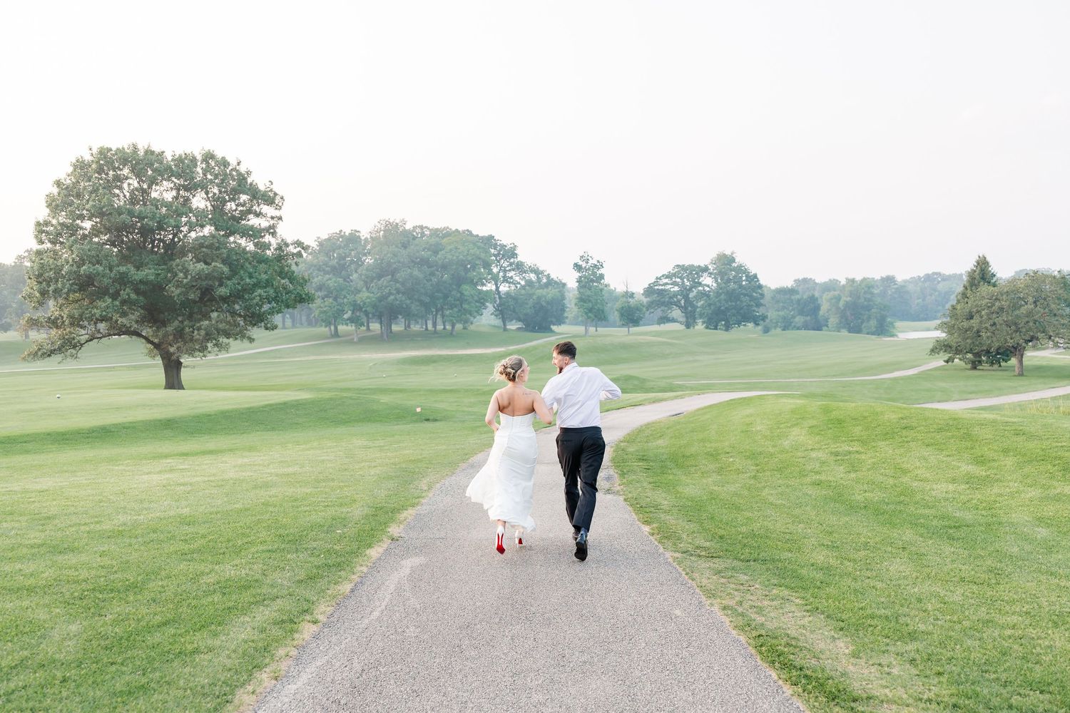Bride and groom run joyfully down a path through a scenic golf course on their wedding day.