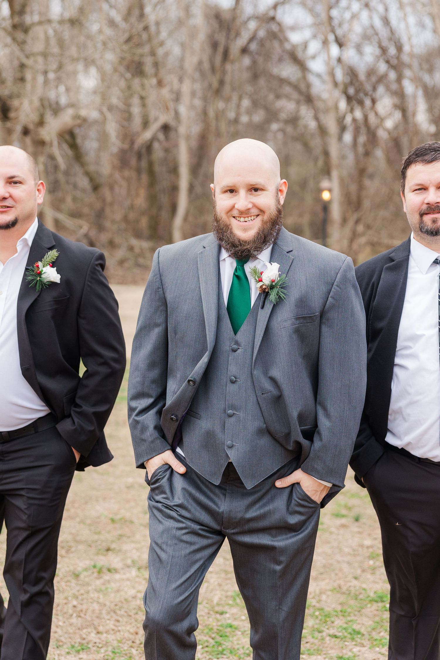 Three groomsmen strike a relaxed pose in formal attire with the center wearing a grey suit and green tie.
