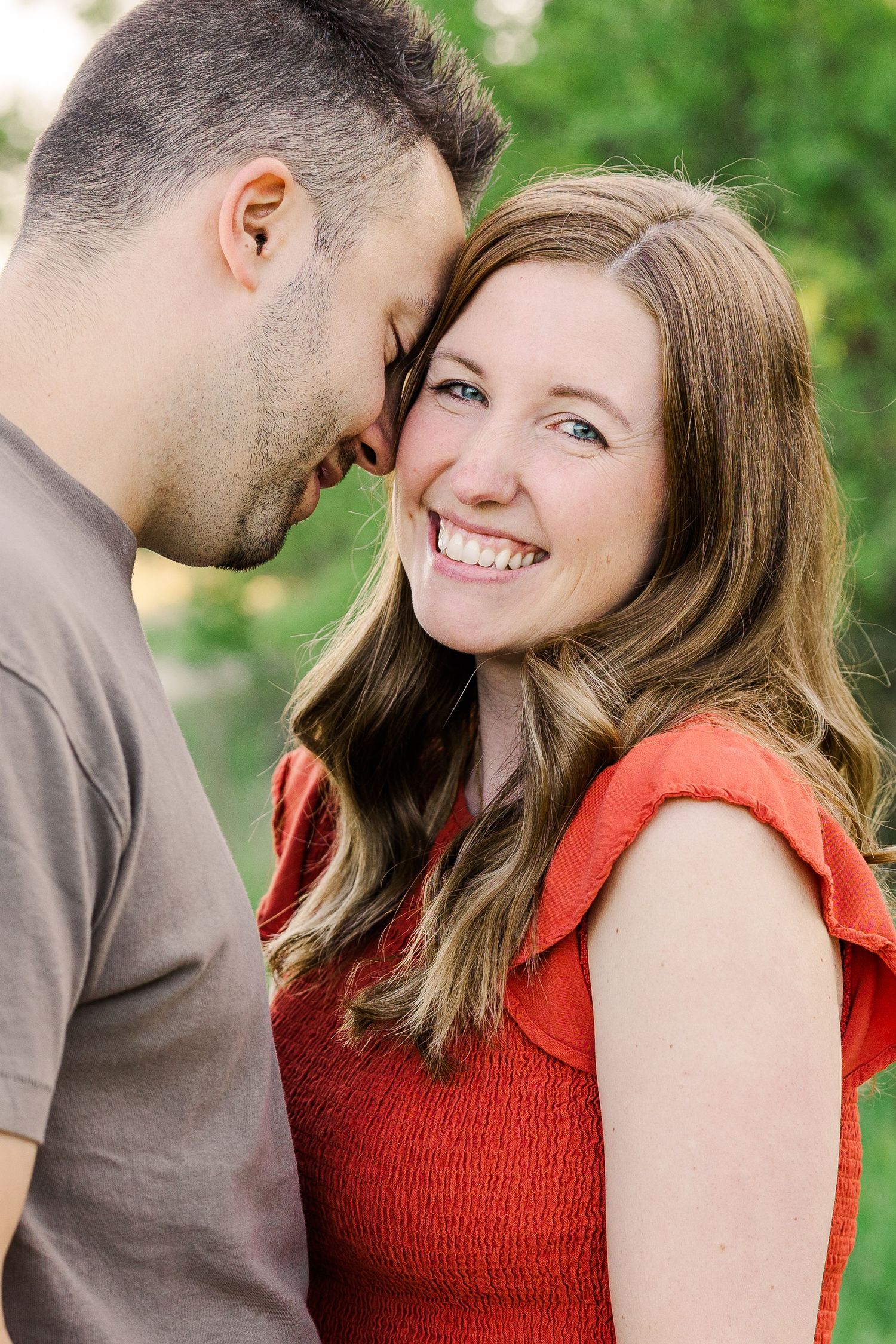A couple shares an intimate moment while smiling together outdoors.