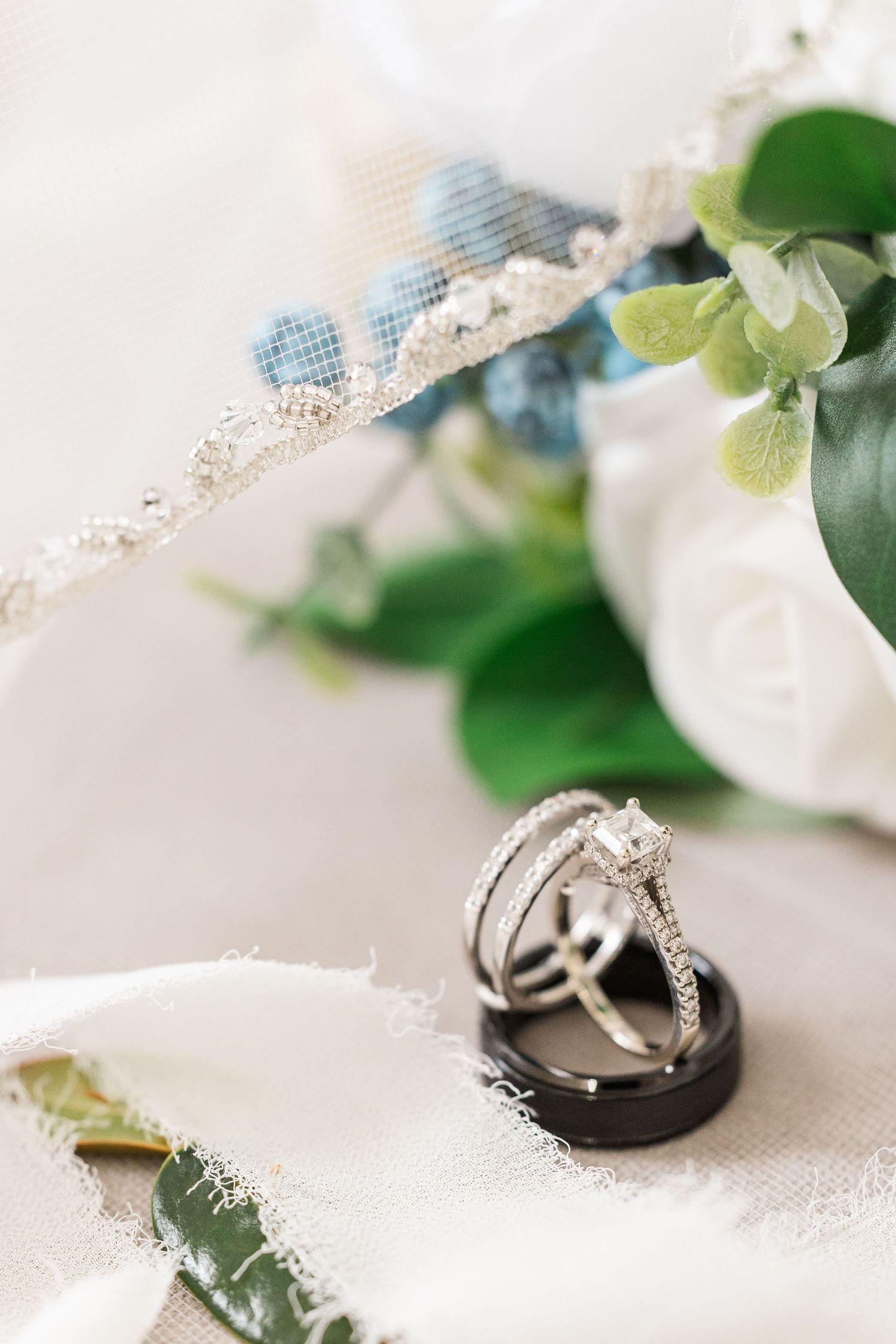 Wedding rings displayed with delicate lace and greenery details on a white surface.