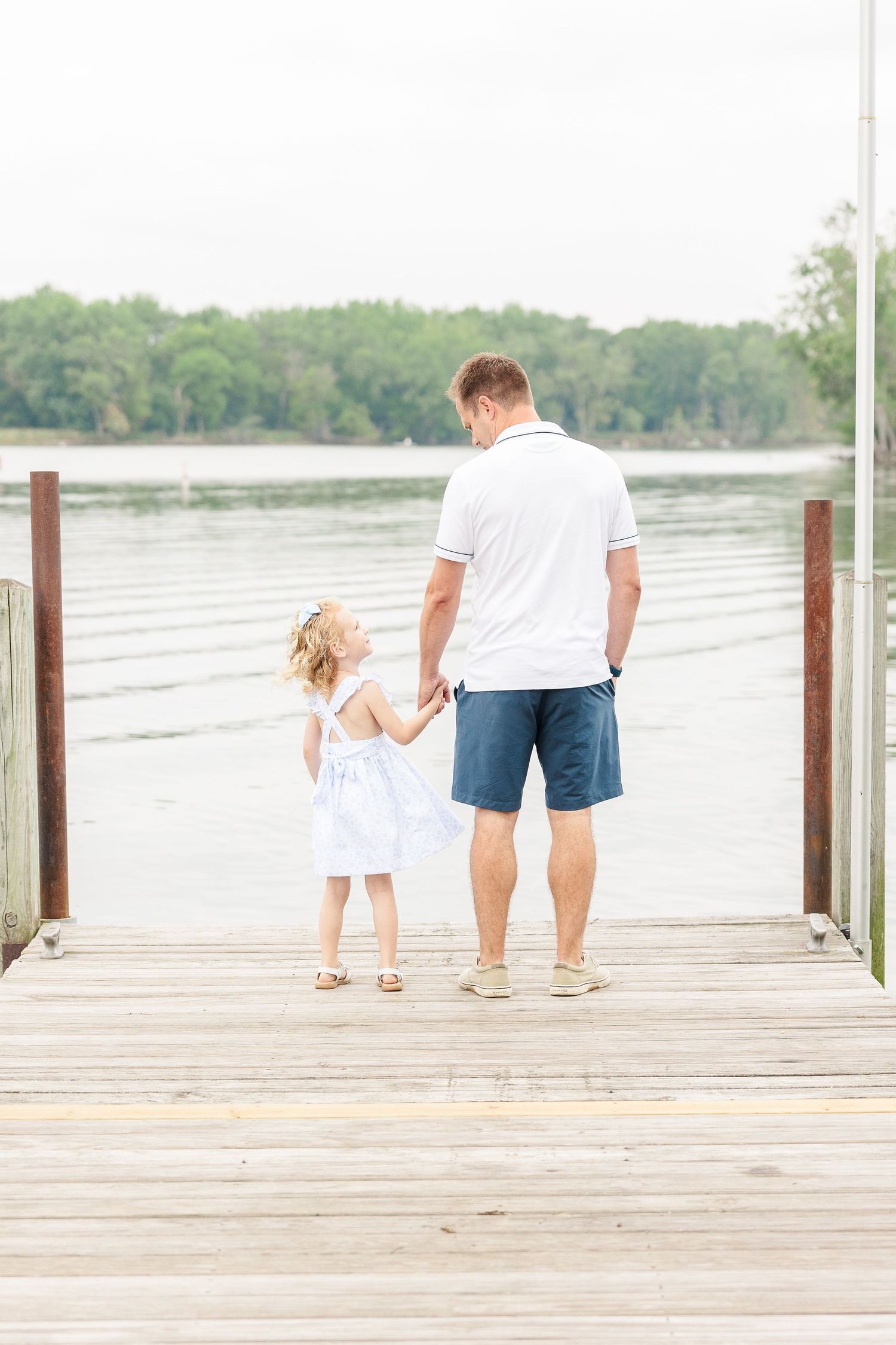 Two people stand together on a wooden dock overlooking a peaceful lake.