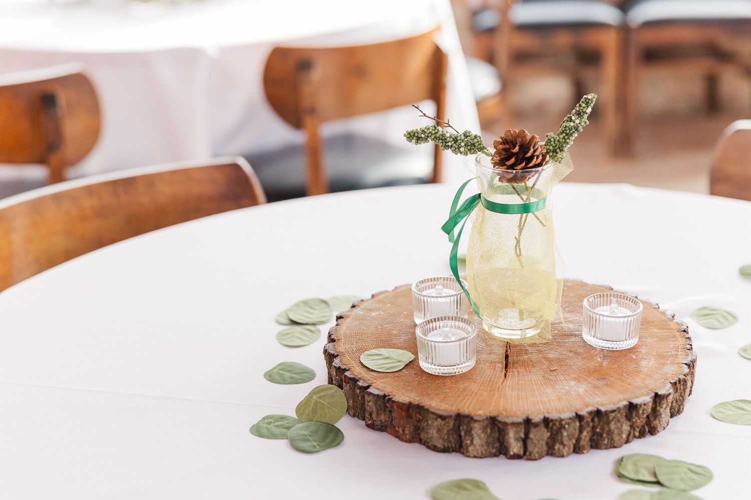 Rustic wedding centerpiece with pinecone and greenery in mason jar on wood slice table decoration.