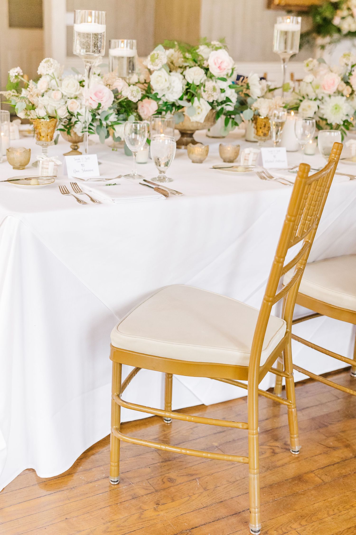 Wedding reception table with gold chiavari chair and white floral centerpieces on crisp white linens.