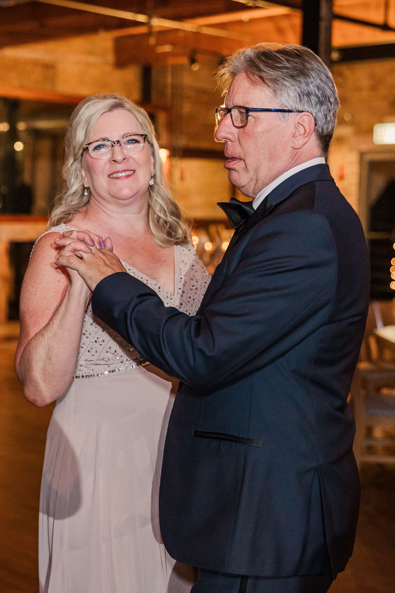 A heartwarming dance moment captured in a rustic venue with exposed brick walls and warm lighting.