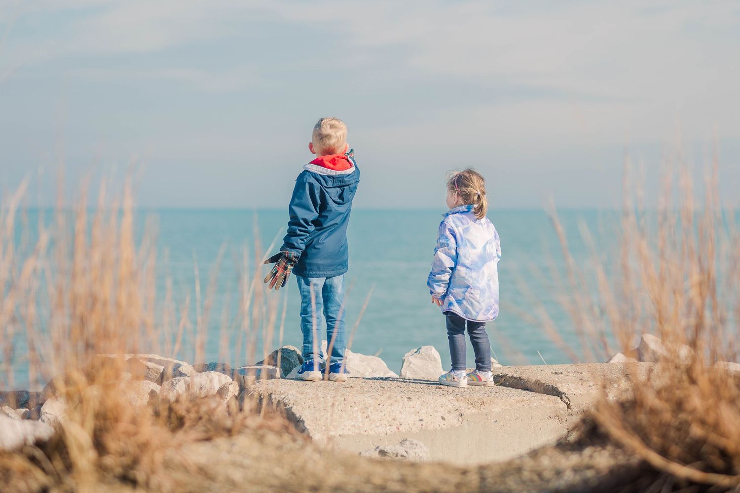 Two people exploring a coastal path with dried grass and ocean views.