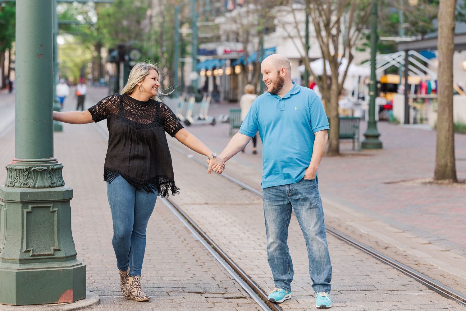 A couple holds hands while walking along trolley tracks on a charming city street.