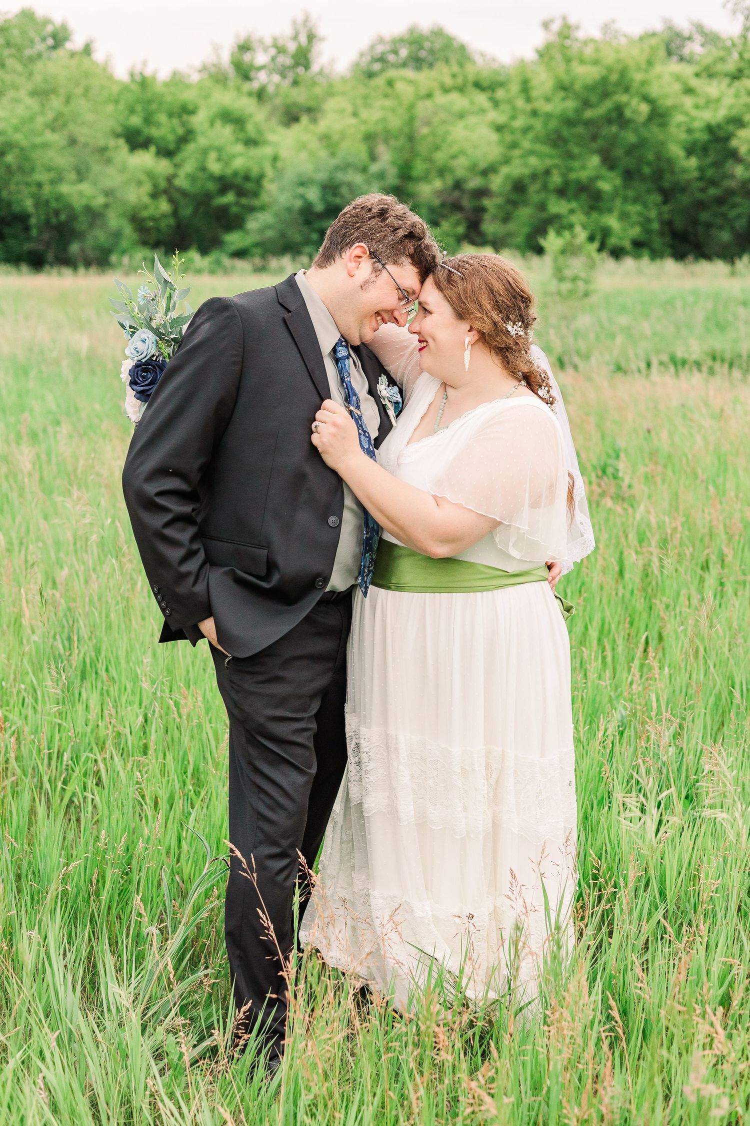 A sweet wedding photo of a couple embracing in a lush green field.