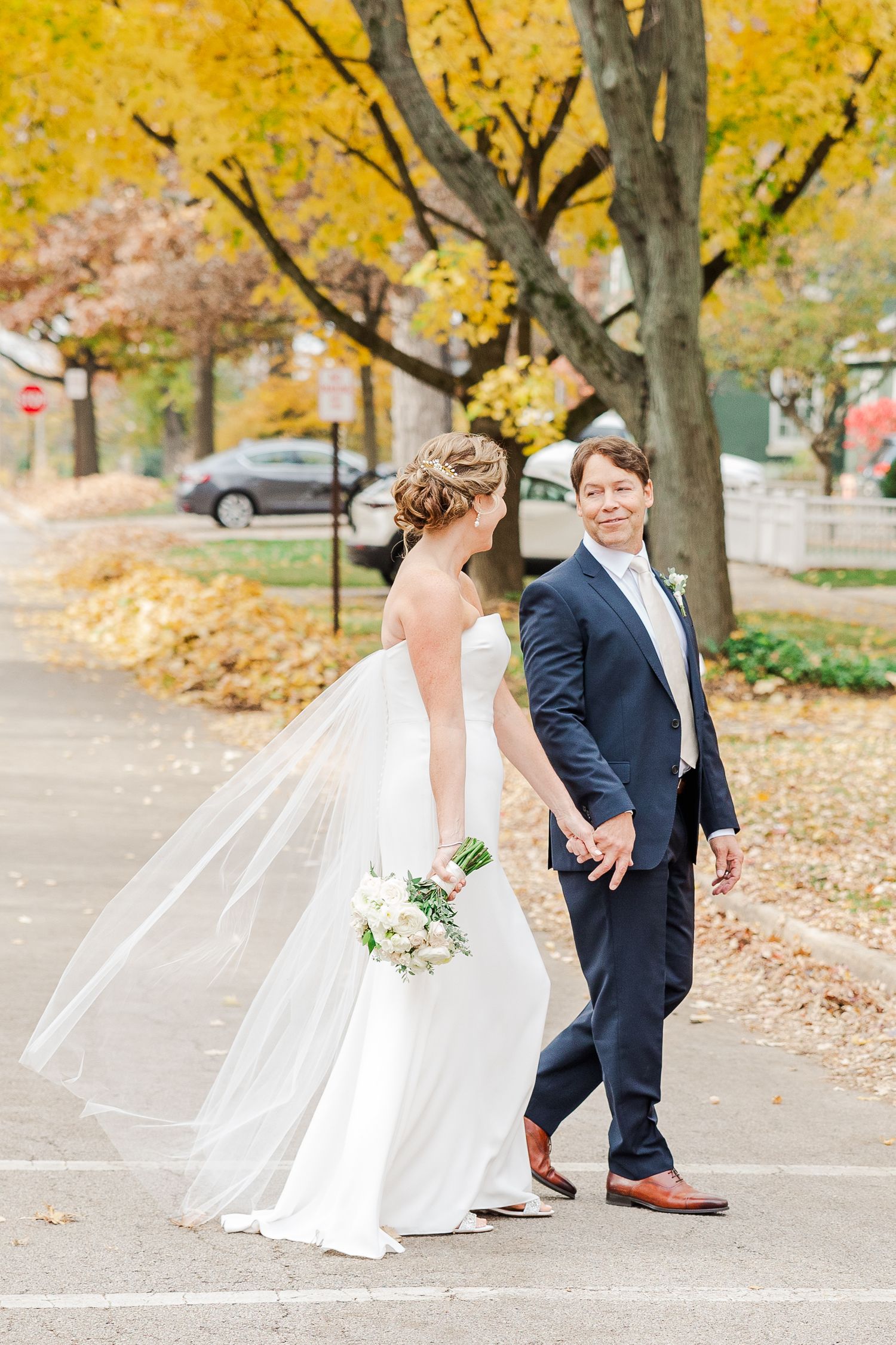 Romantic wedding moment captured on street with autumn leaves falling.