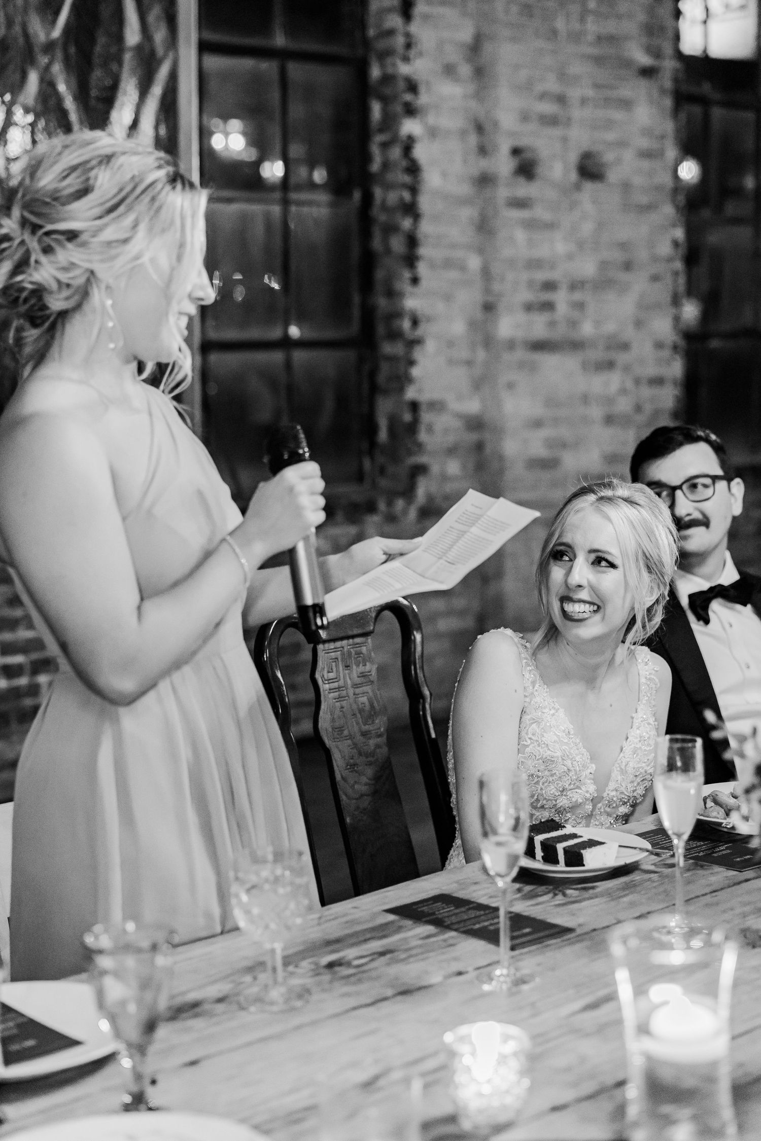 Wedding reception speech moment in rustic brick venue with candlelit table setting.