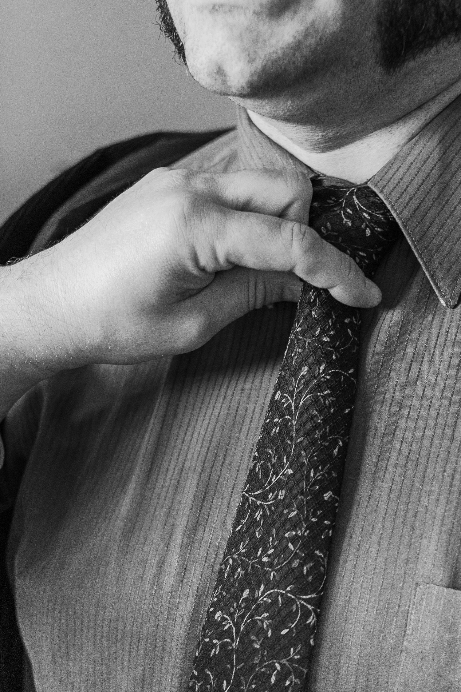 Black and white close-up of hands adjusting a patterned necktie.