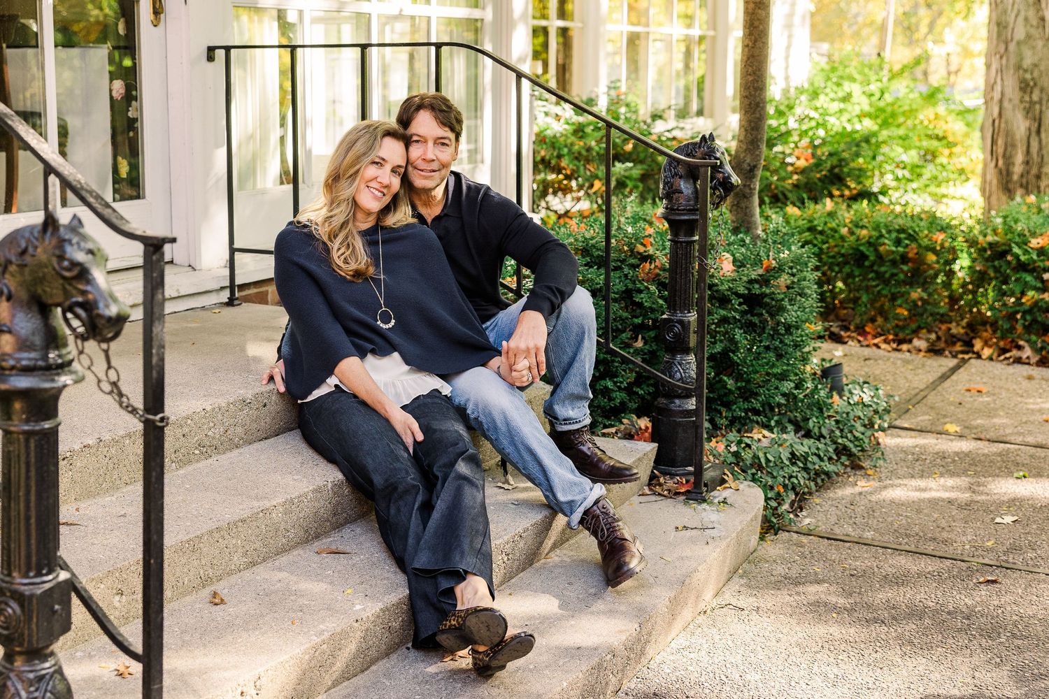Couple in dark sweaters sitting together on stone steps with iron railing.