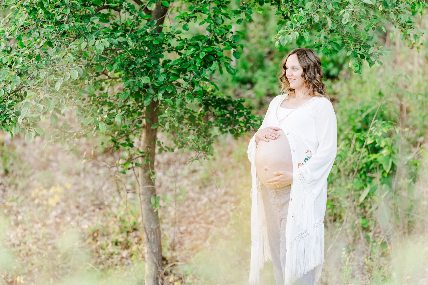 Mother standing in spring greenery during golden hour maternity photos at Veterans Acres Nature Preserve.