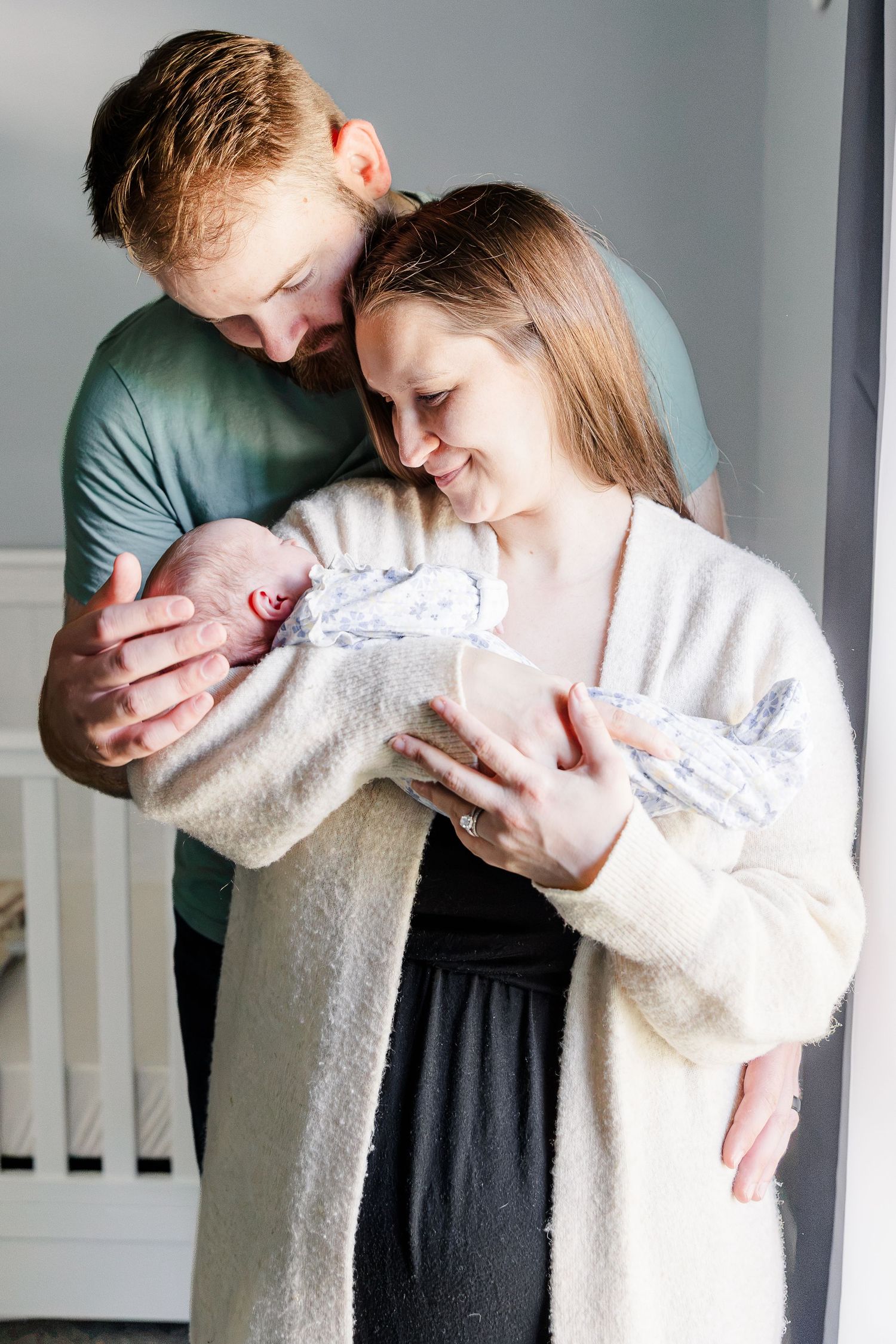 New parents lovingly gaze at their swaddled newborn baby together in a softly lit nursery.