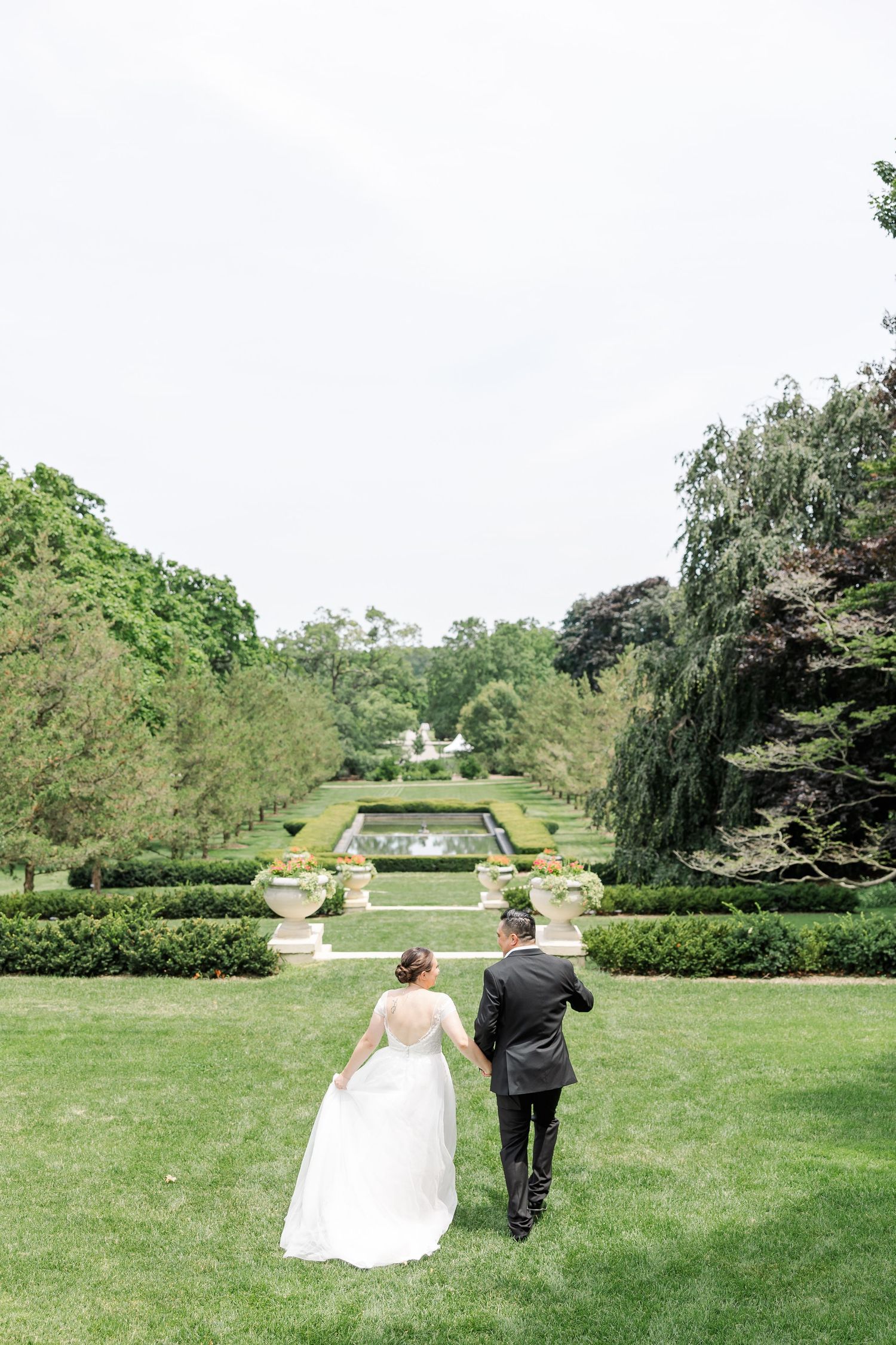 Monika and Rafael walking hand in hand toward the formal gardens during their wedding portrait session.
