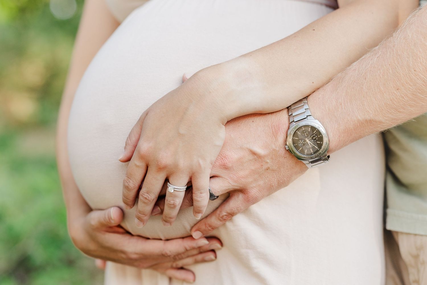 Two sets of hands hold each other tenderly against a soft green outdoor background.