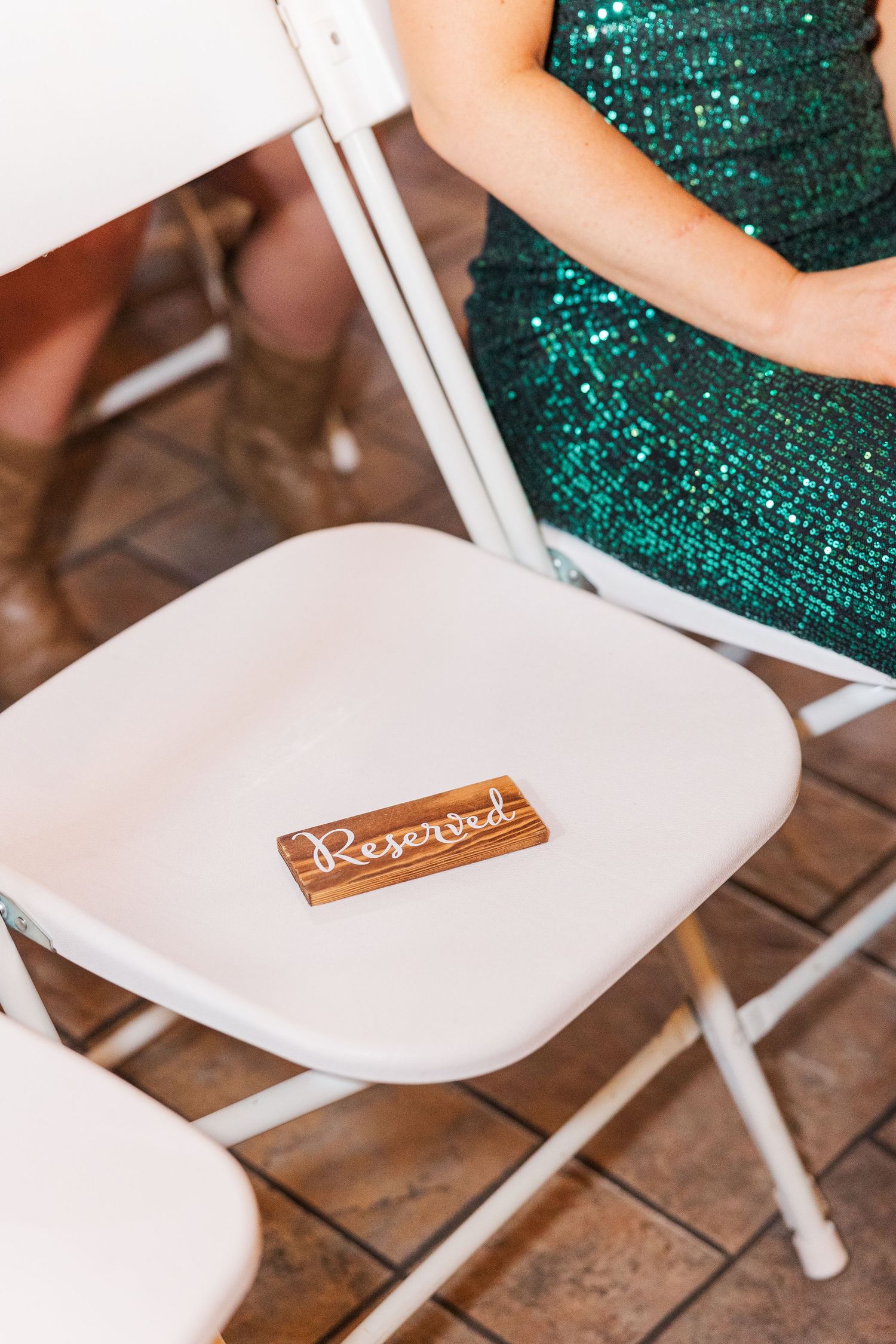 Reserved sign on white folding chair next to person wearing sparkly green dress.