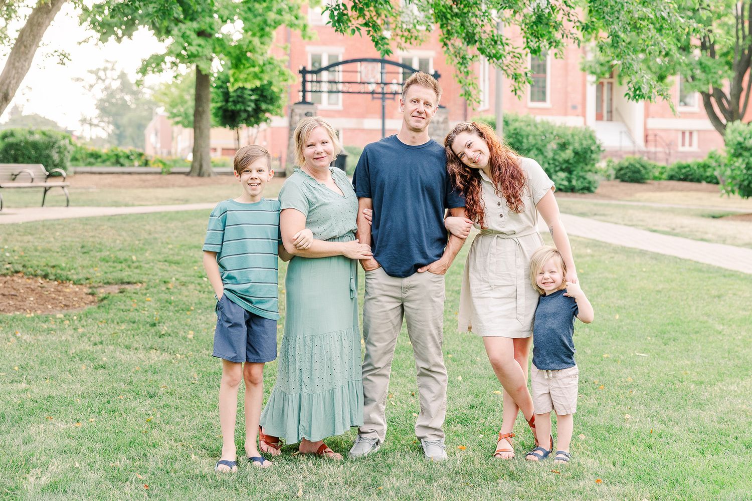 A group poses together on a sunny day in front of a red brick building surrounded by green grass.