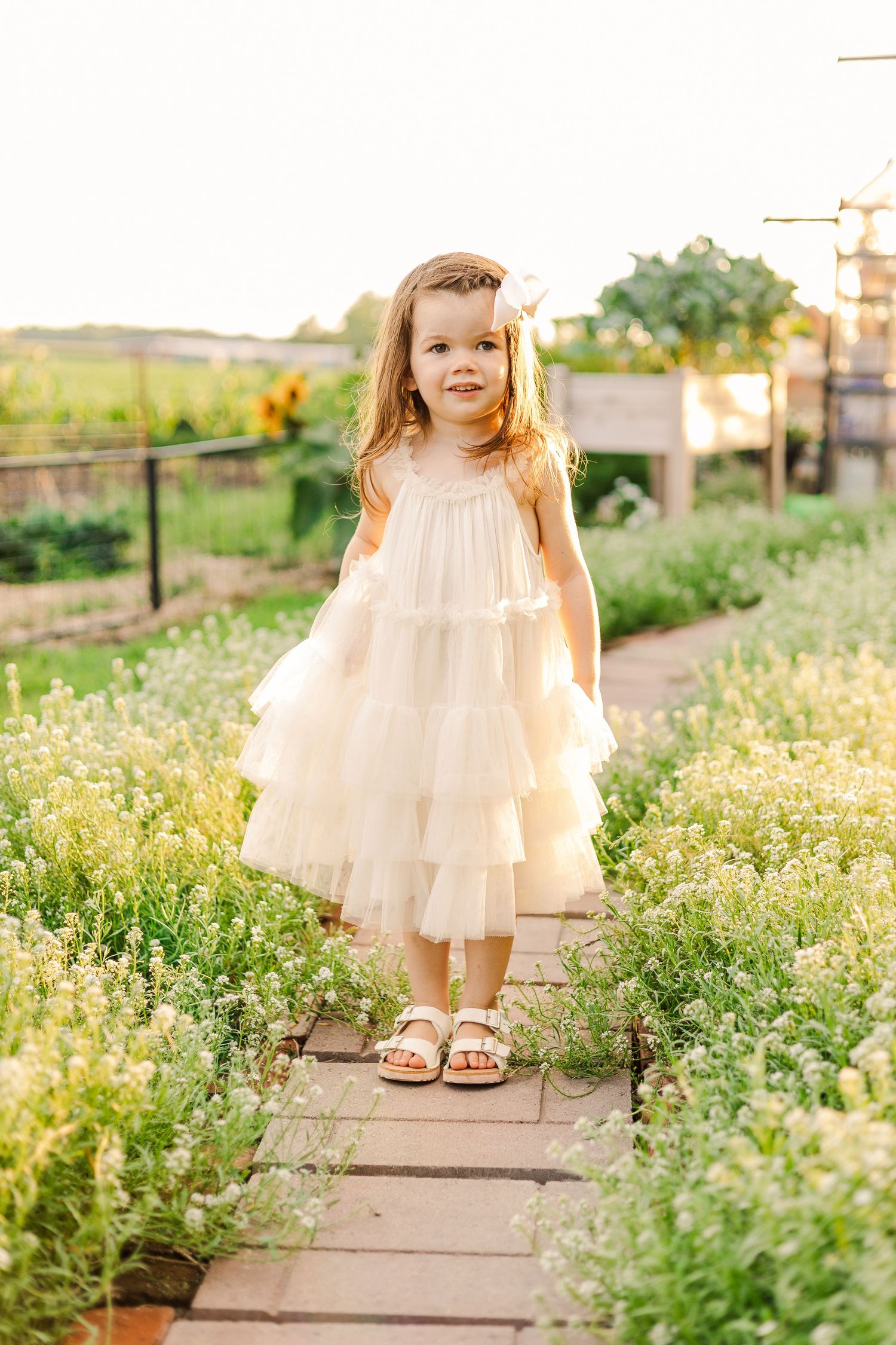 A whimsical garden moment captured with a flowing white dress amid blooming summer flowers.