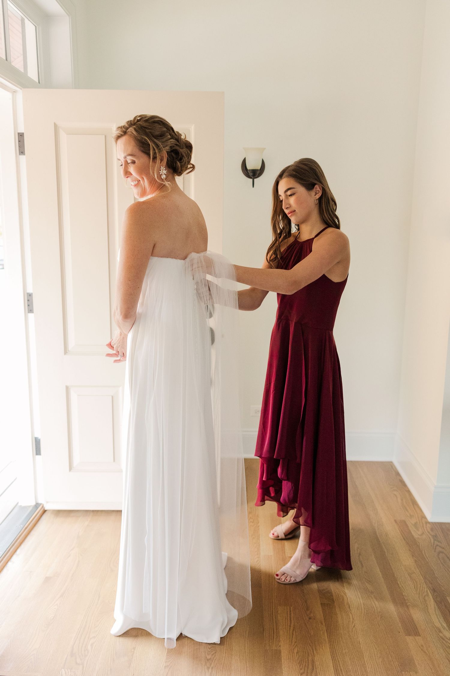Wedding dress preparation scene with attendant helping adjust the gown.