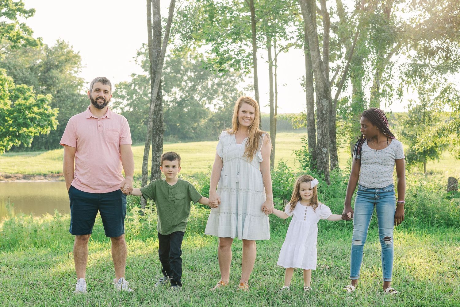 Group standing together in a sunlit meadow during golden hour among trees.