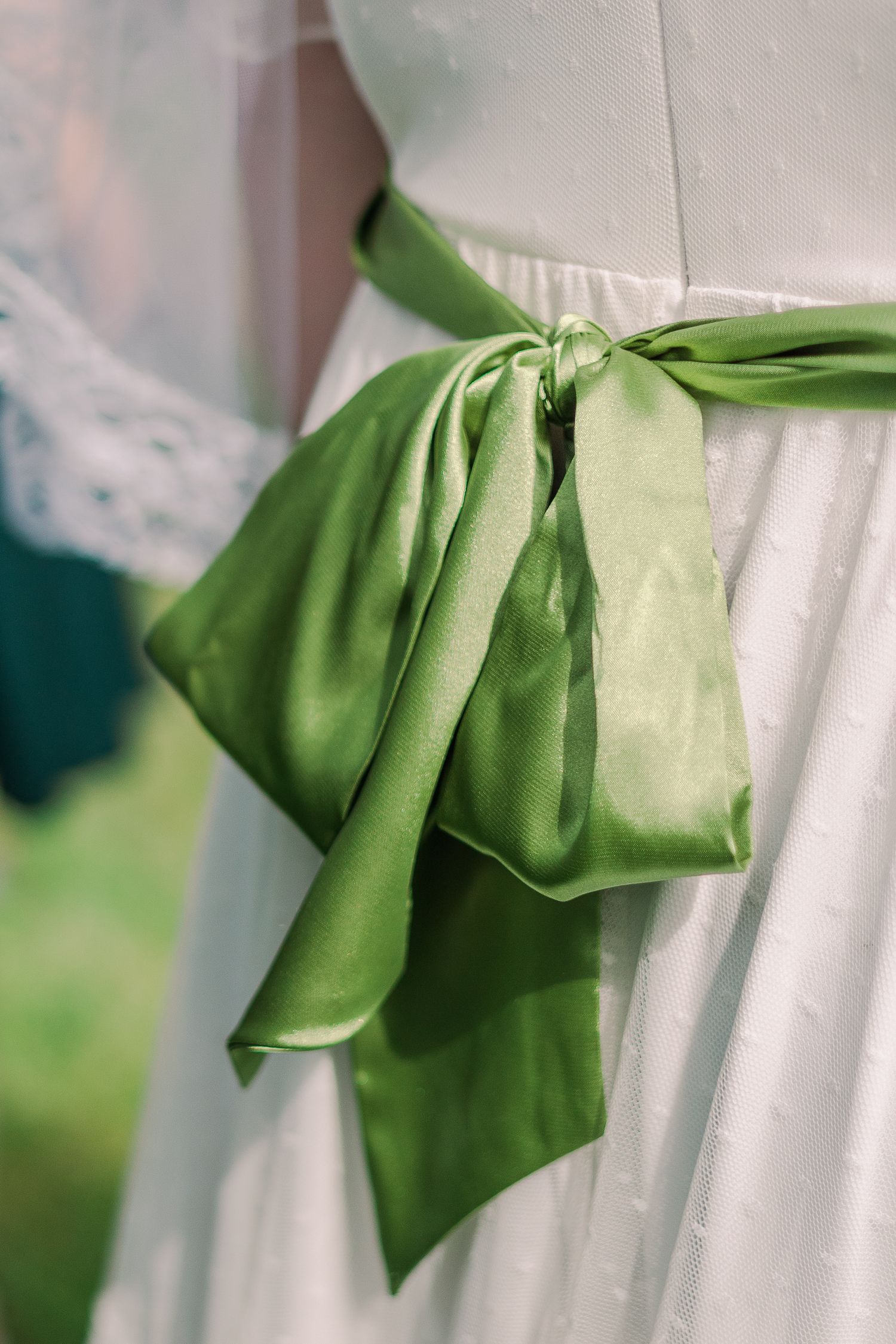 Close-up of emerald green satin sash tied in bow on white dress.