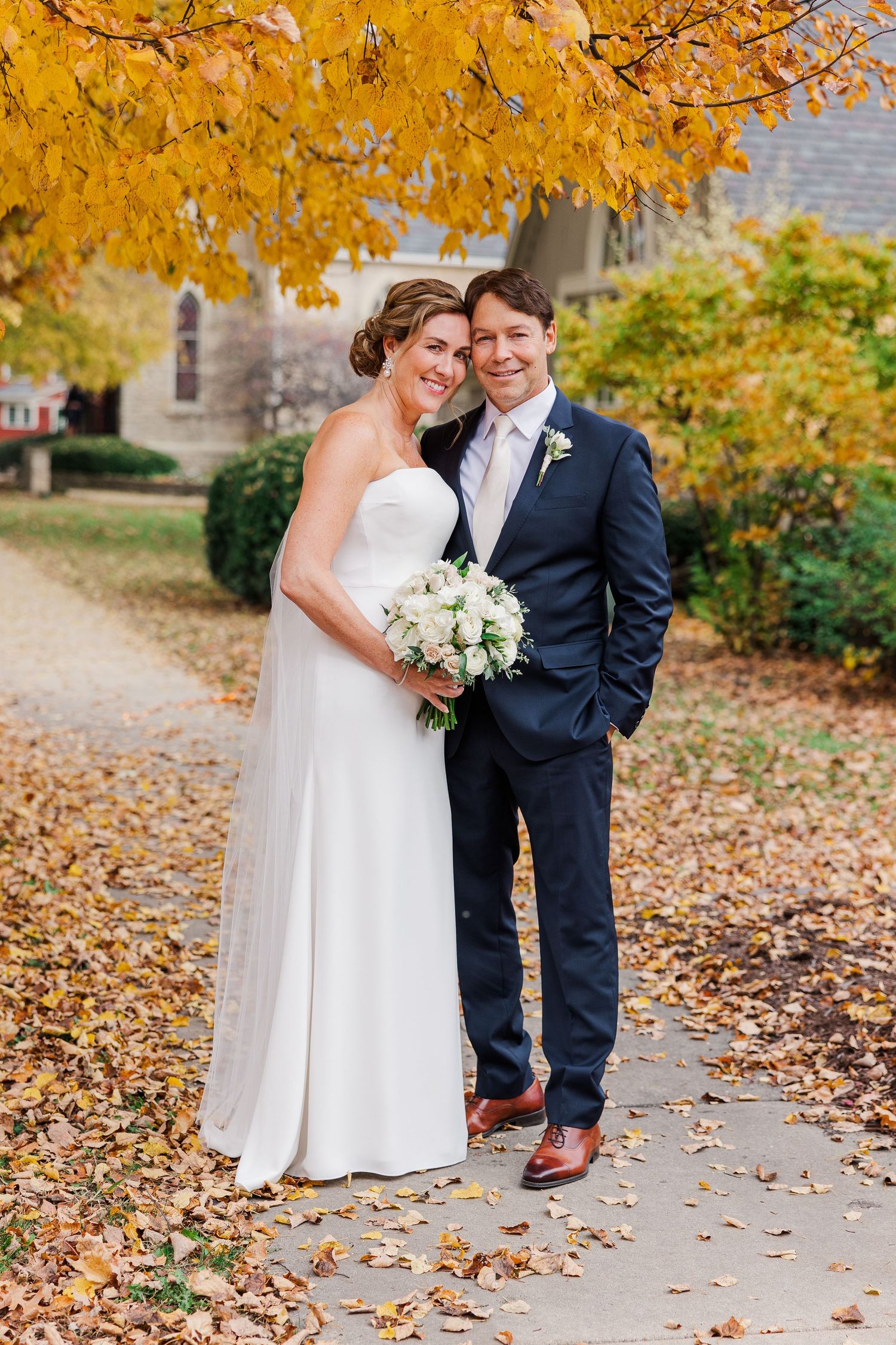 Full-length wedding portrait of couple on path with fall foliage.