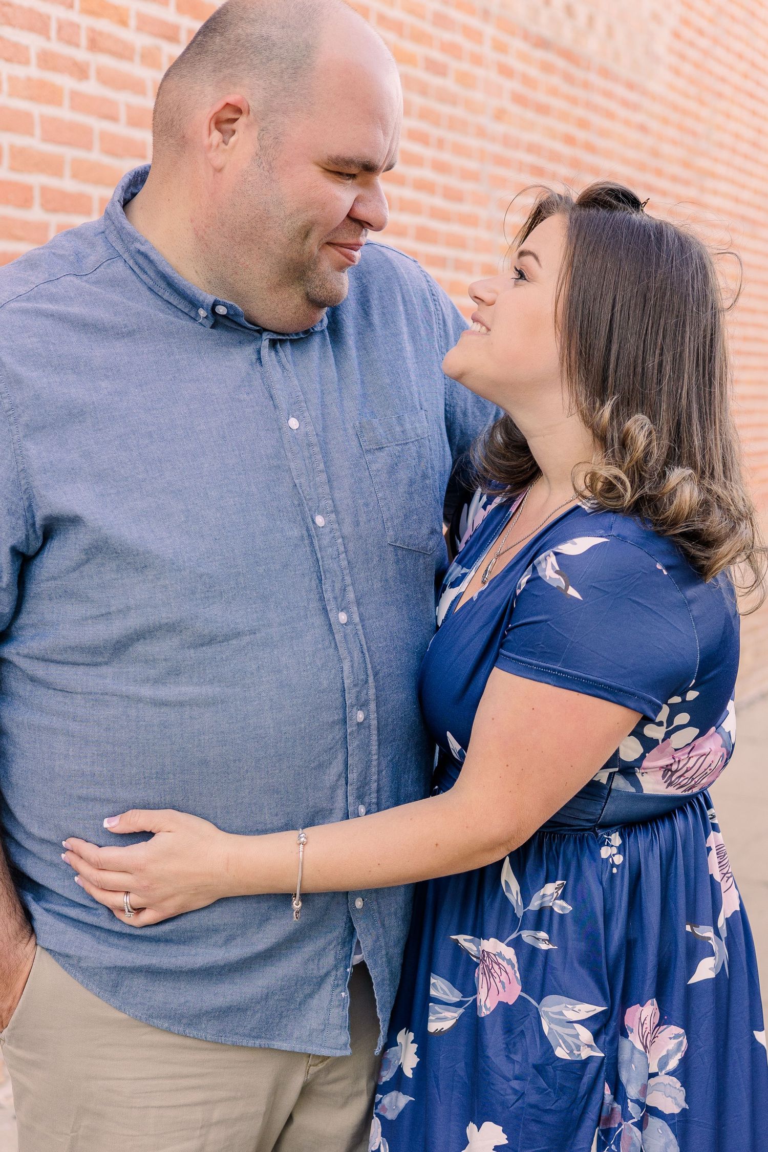Couple in coordinating blue outfits sharing loving moment against brick wall.