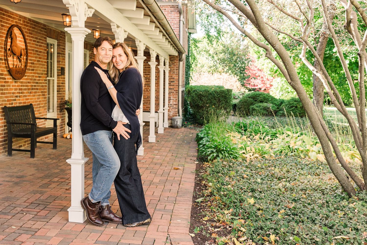 Romantic couple embracing on a brick porch with white columns and garden background.