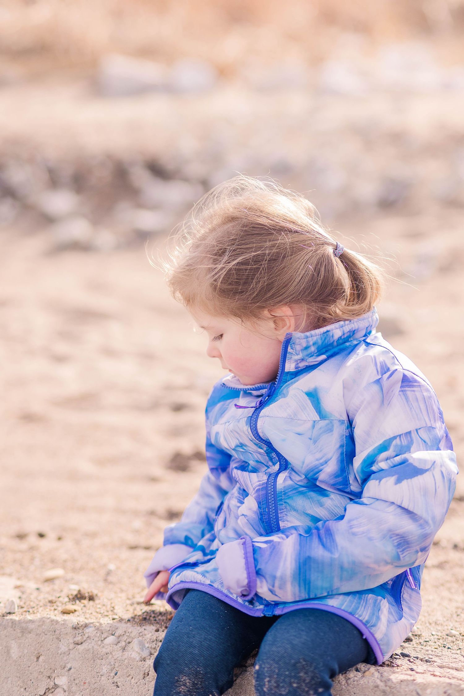 Someone in a blue patterned jacket sits quietly looking down at the sand.