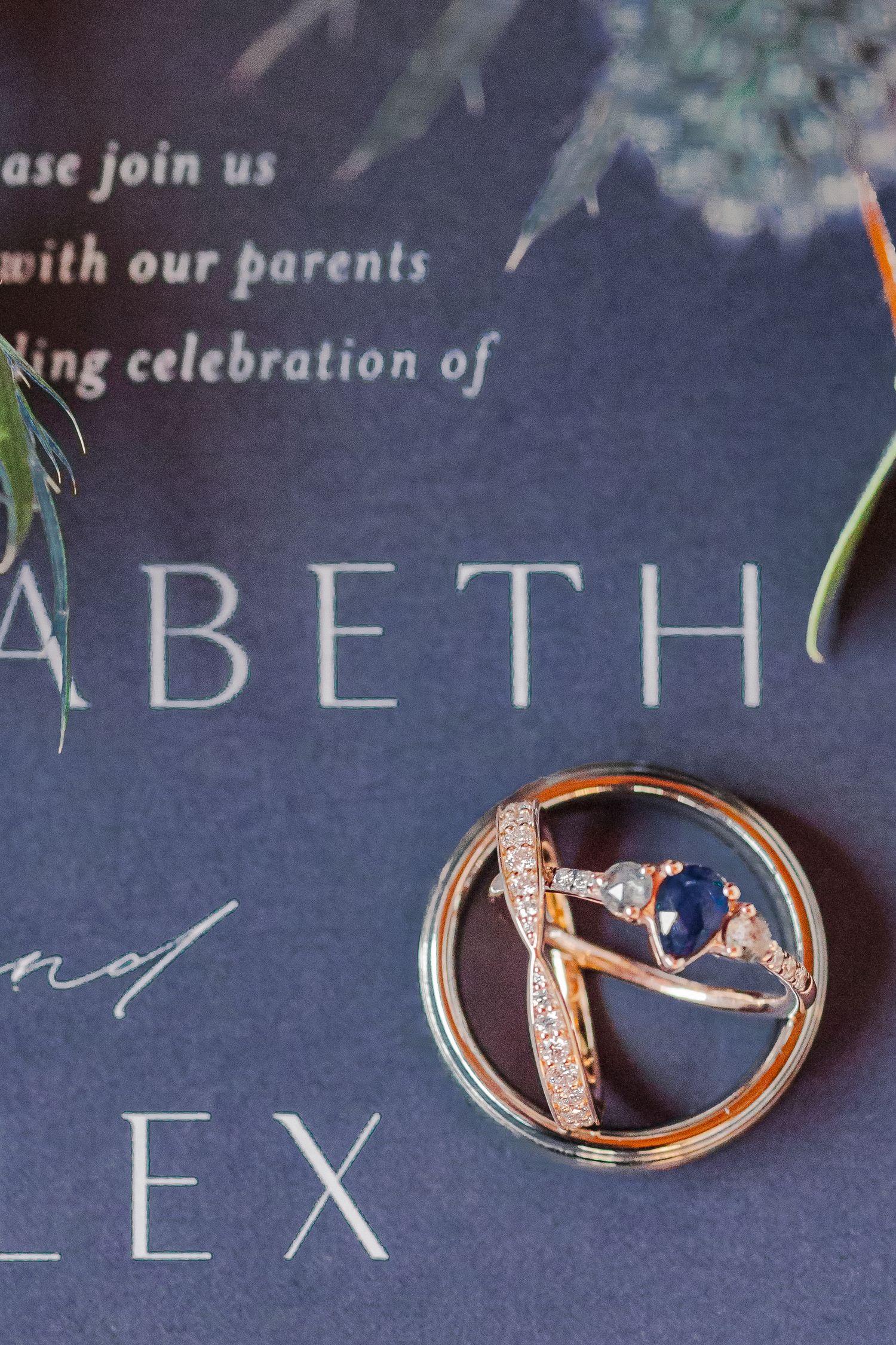 Wedding rings artistically arranged on a navy blue invitation showing the names Elizabeth and Alex.